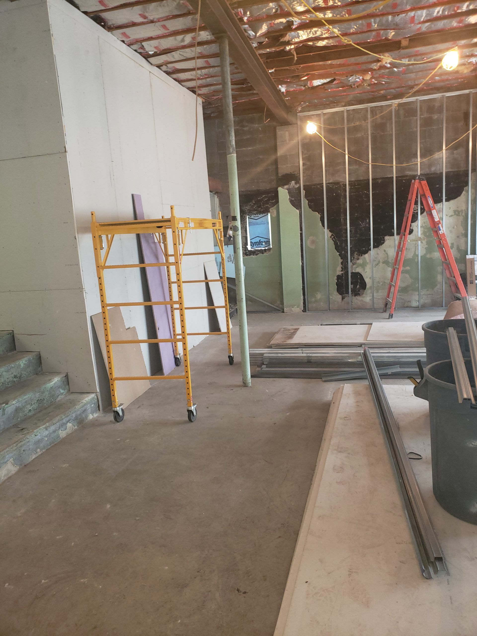 Construction site: drywall, scaffolding, exposed walls, concrete floor, stairwell, overhead supports.