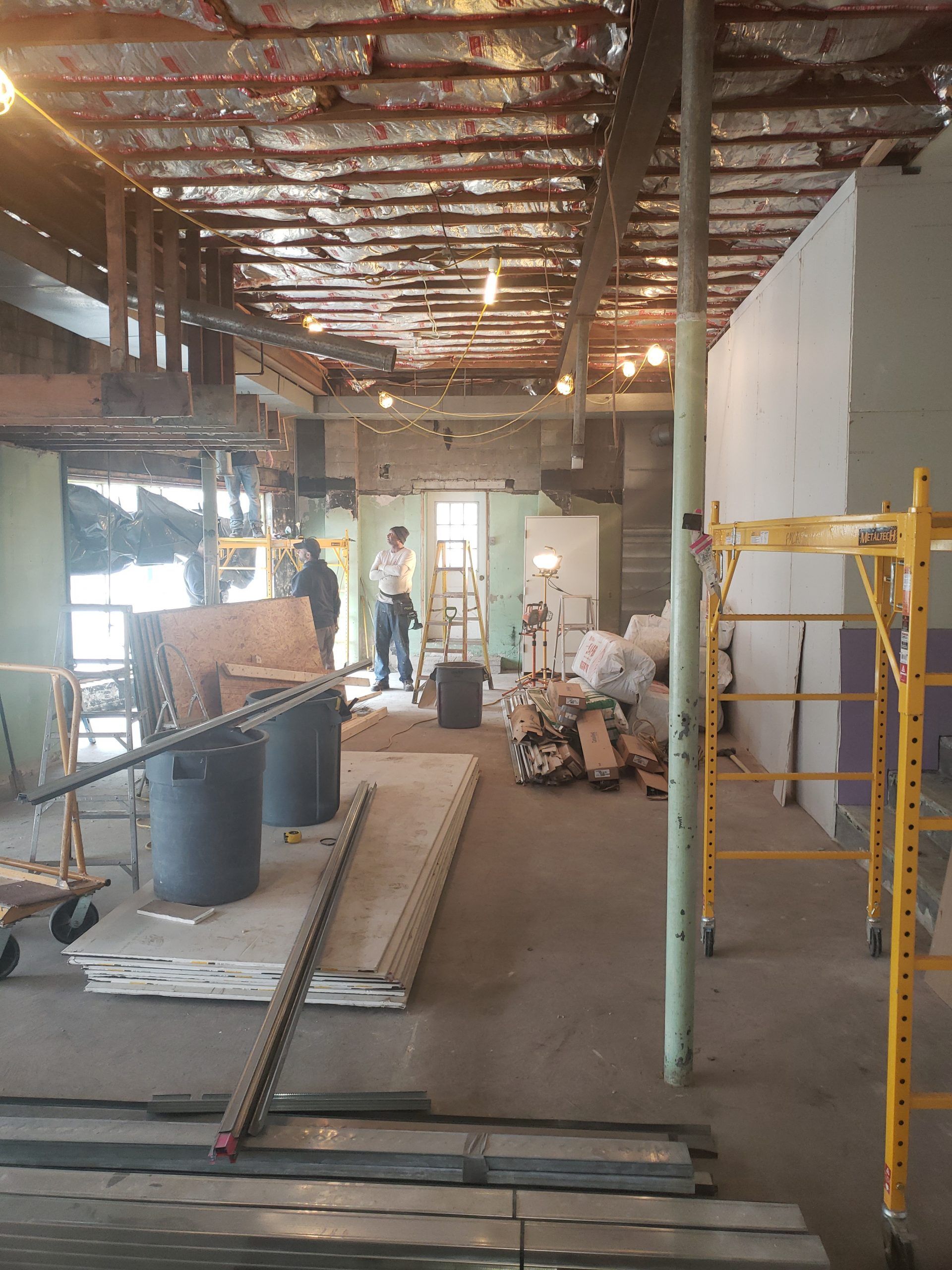 Interior view of a construction site: exposed ceiling beams, scaffolding, and workers.