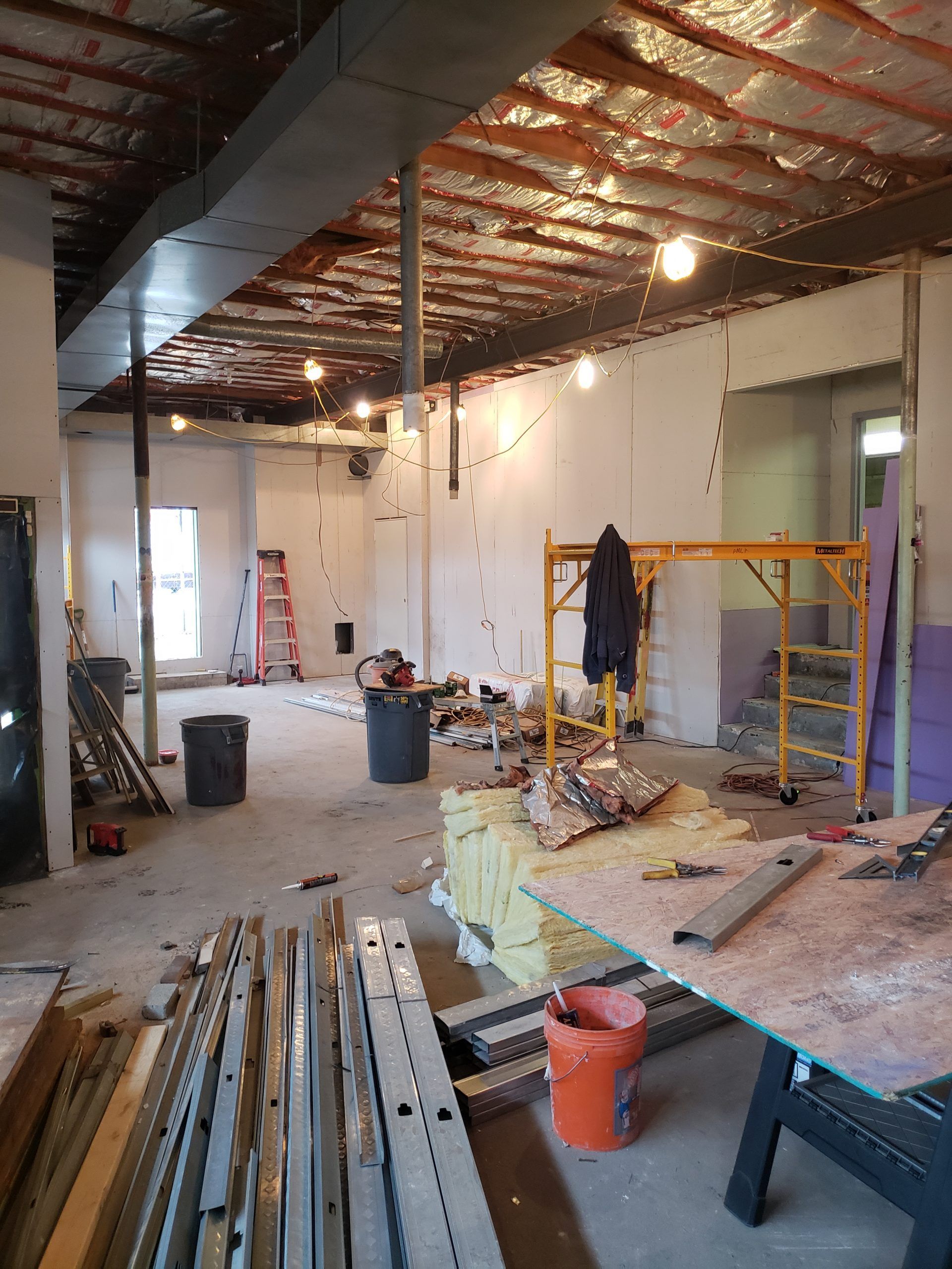 Interior construction site with exposed ceiling, scaffolding, and scattered materials.