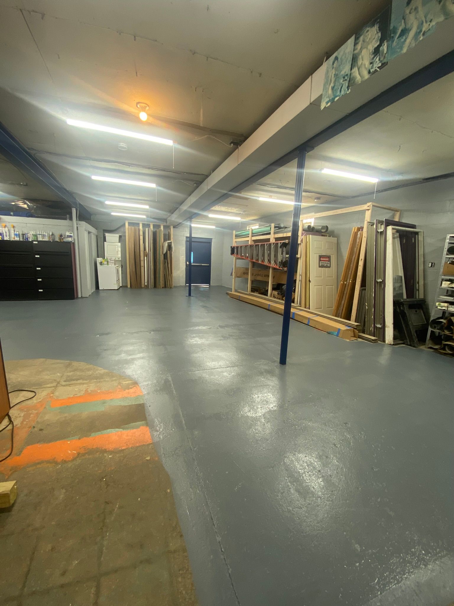 Warehouse interior with gray floor, various stored materials, and overhead lighting.