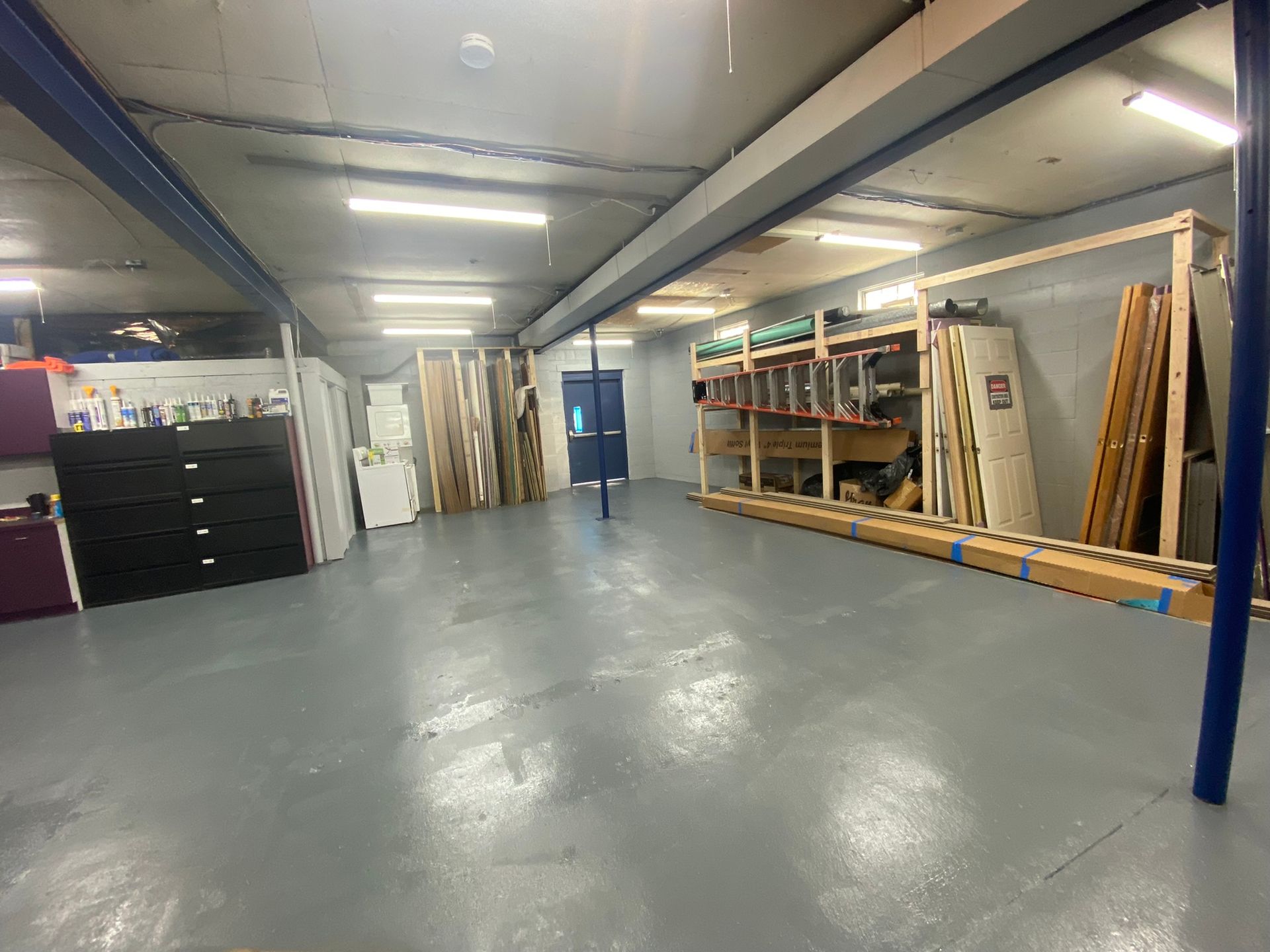 Spacious storage room with gray floor, various shelving units, doors, and building materials.