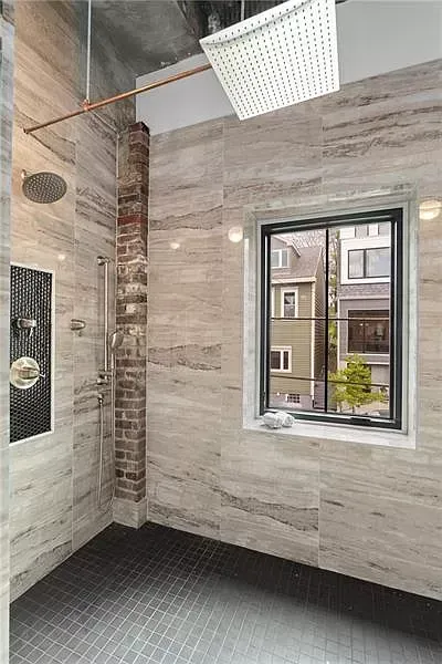 Bathroom with tiled walls, exposed brick column, and a window overlooking a street.