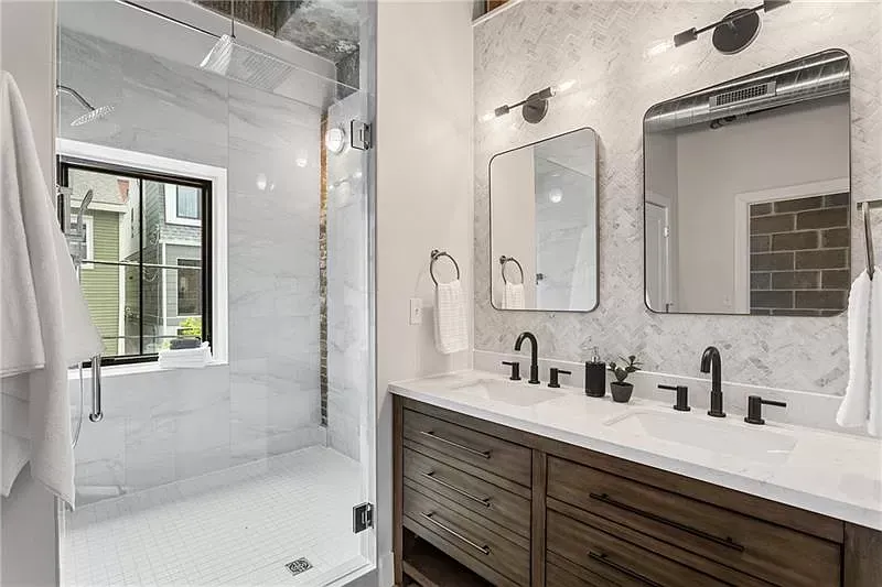 Modern bathroom with marble shower, double vanity, dark wood cabinetry, and window.