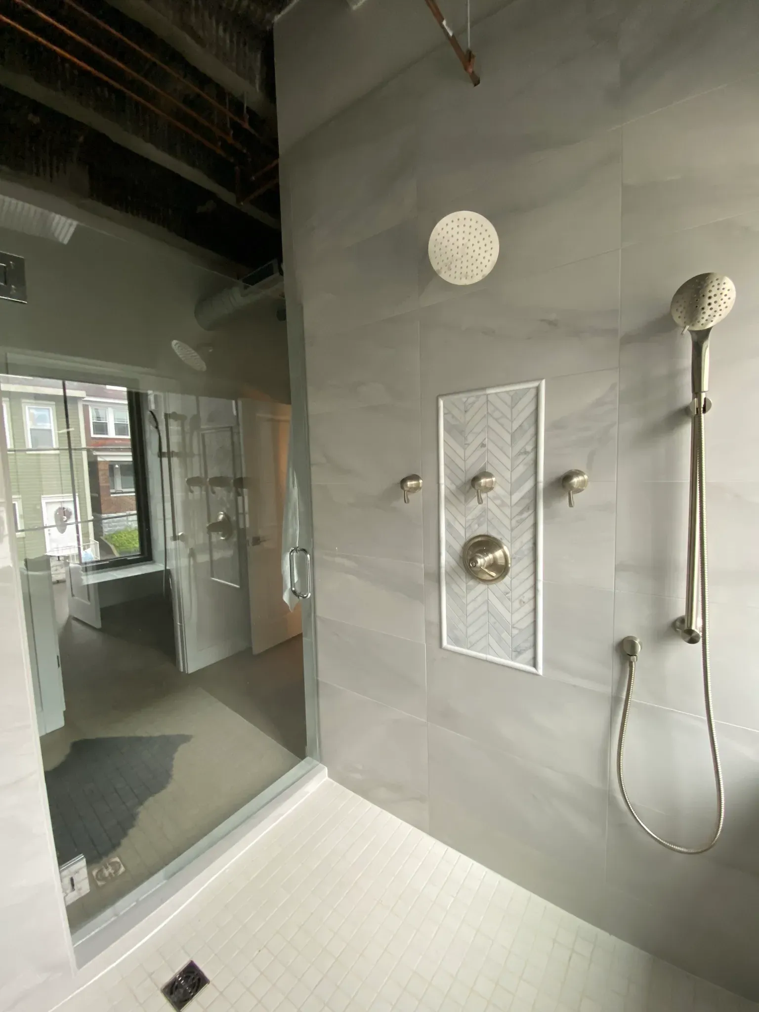 Modern bathroom with grey marbled tile walls, glass shower door, and brushed nickel fixtures.