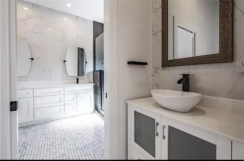 Bright, modern bathroom with white cabinets, marble-like wall, and a black faucet on a vessel sink.