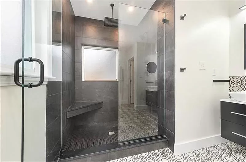 Modern bathroom with dark tile shower, glass door, and patterned floor.