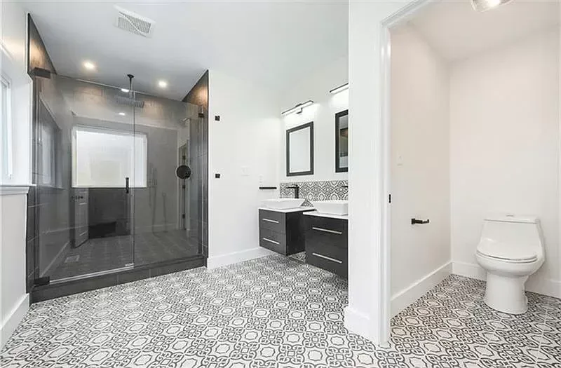 Modern bathroom with glass shower, patterned floor, dual vanity, and toilet.
