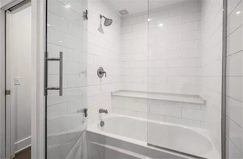 Modern white tiled bathroom with a glass shower enclosure and a bathtub.