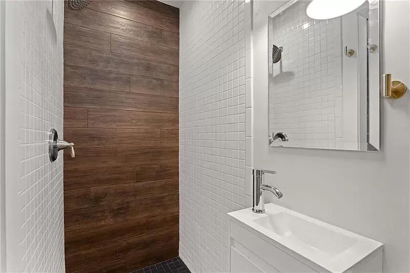 Small bathroom with wood-look shower wall, white tile, and a white sink.