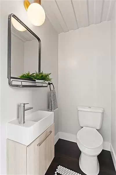Small, modern powder room with white walls, dark floor, a toilet, and a sink with a mirror and lighting.