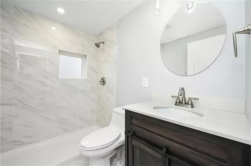 Bathroom with white marble tiled shower and vanity with dark brown cabinet.