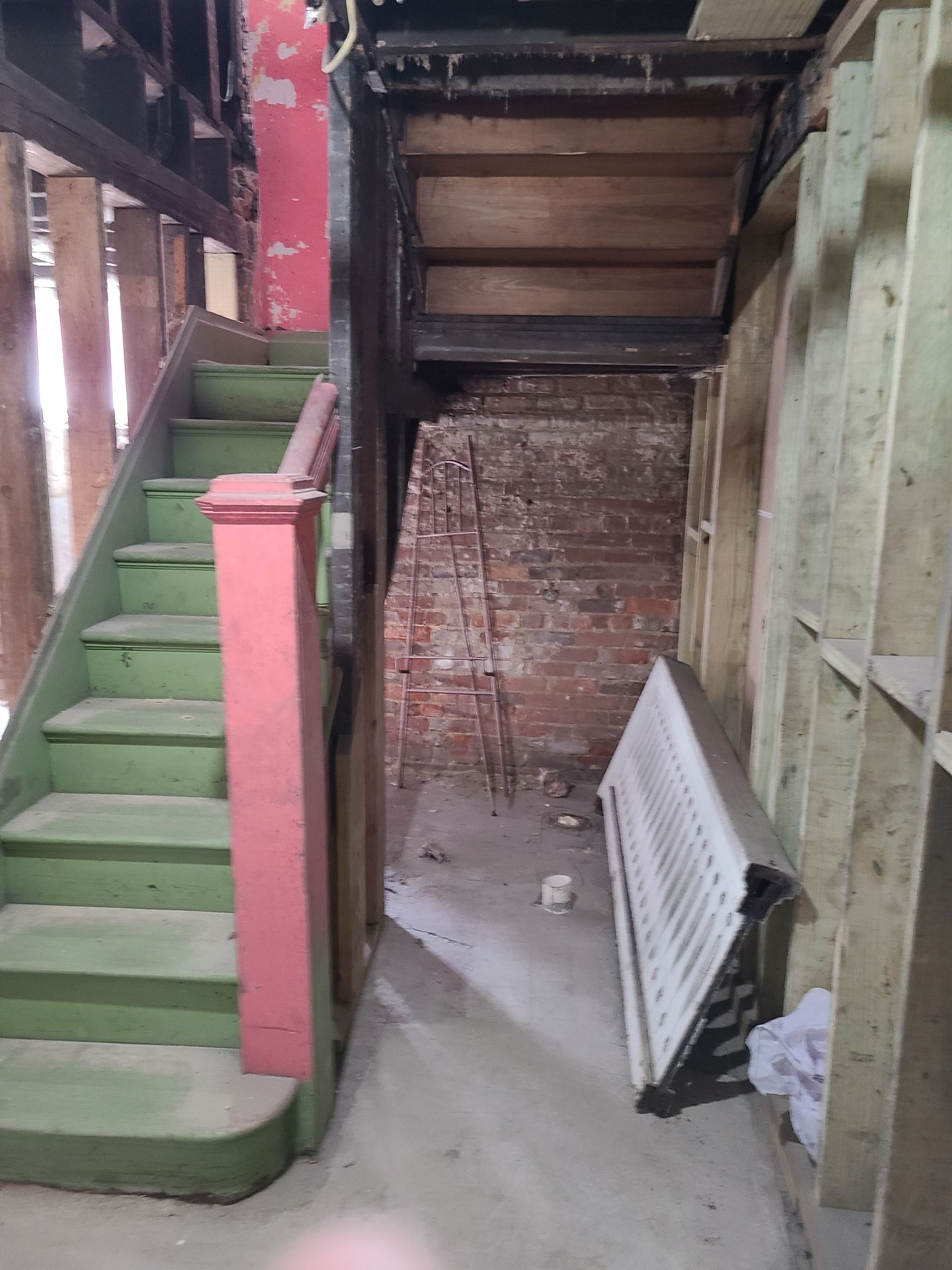 Interior hallway with exposed brick, staircase, and a radiator, during renovation.