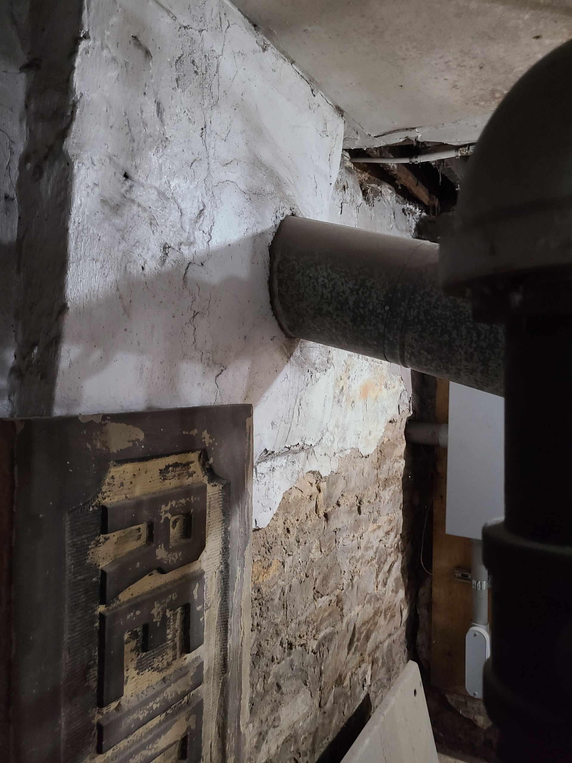Basement wall with a pipe passing through; brick visible, some white plaster.