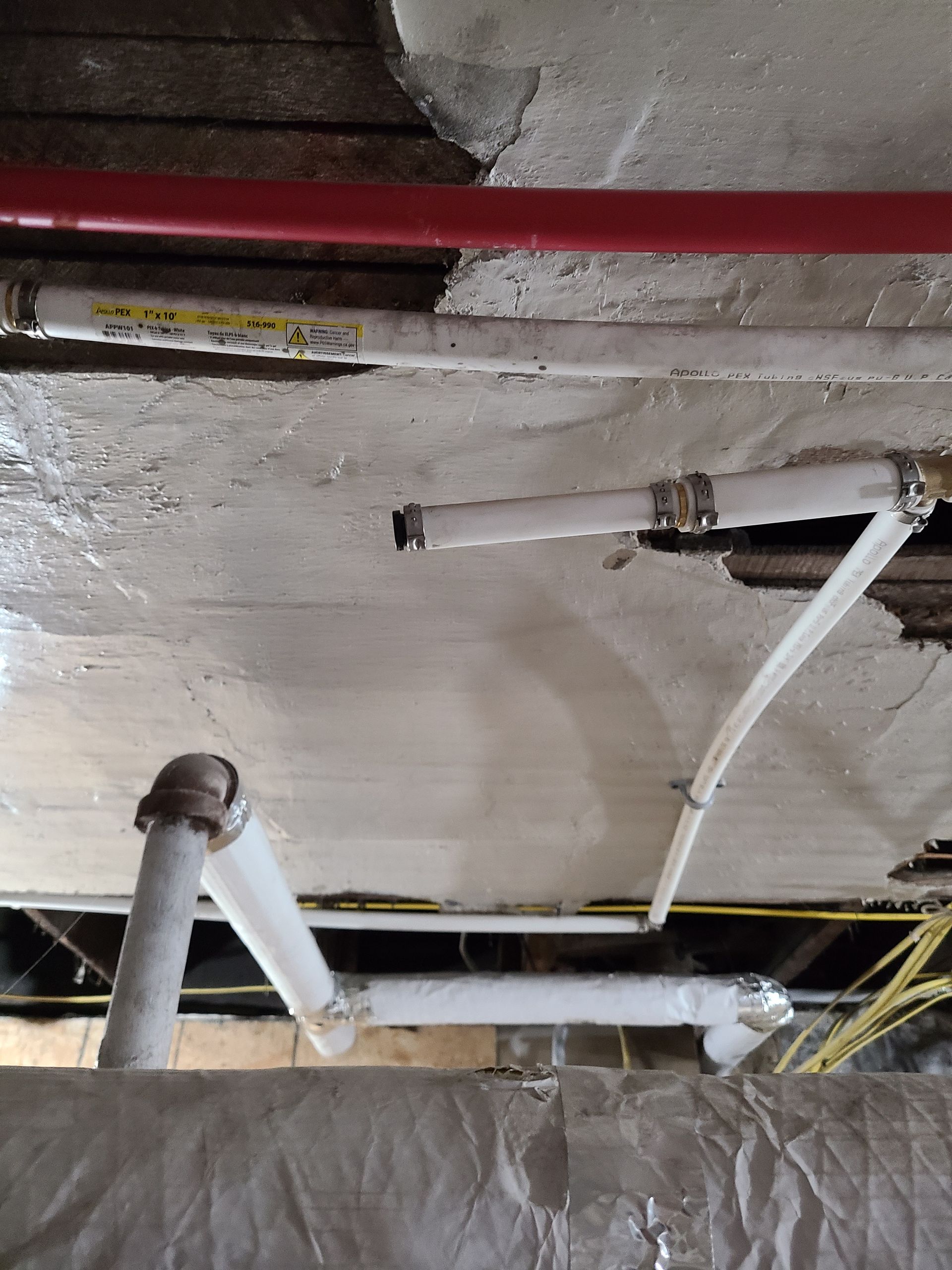 Pipes and wiring exposed on a ceiling. White and red pipes, yellow wires. Damaged ceiling.