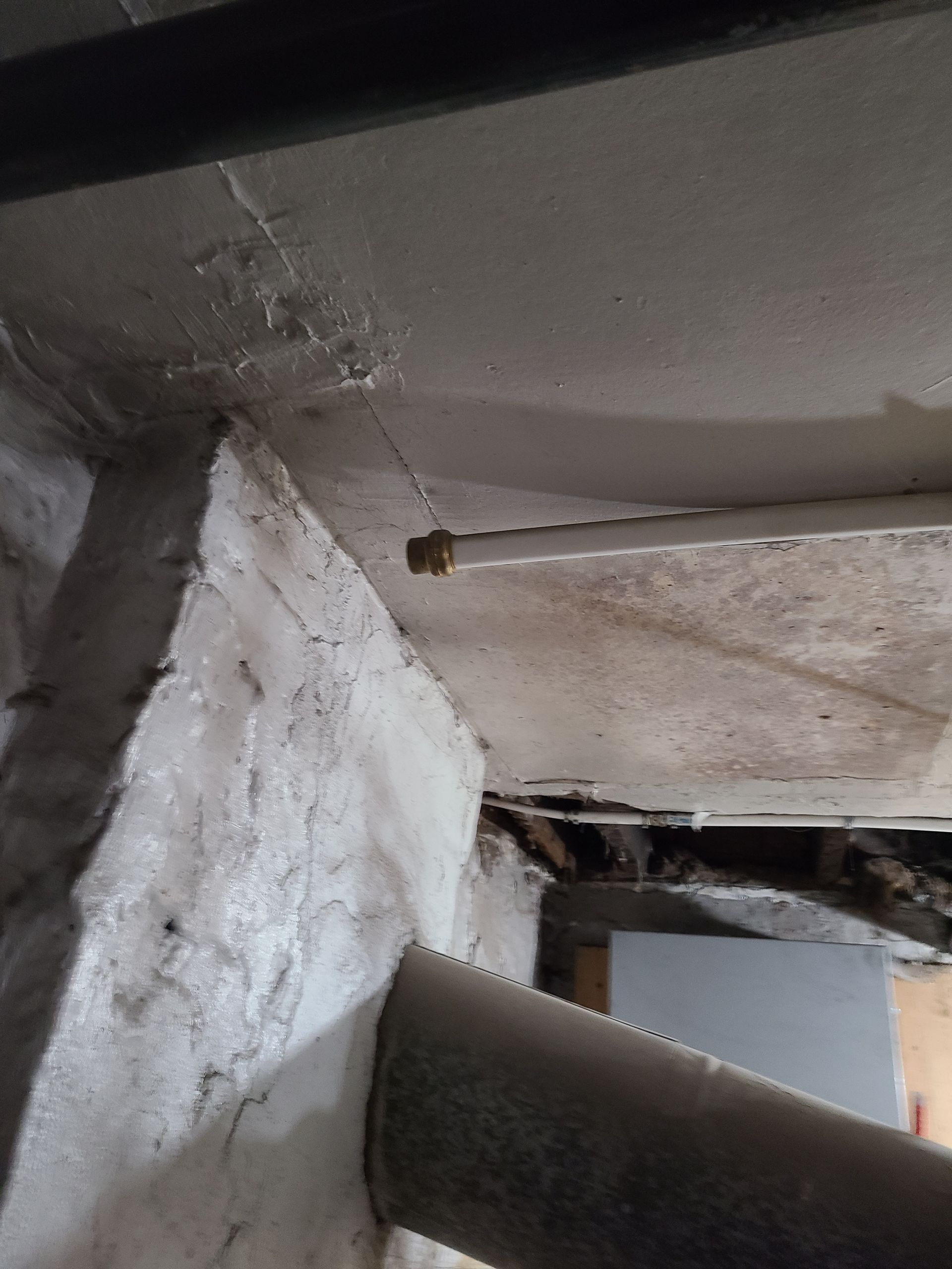 White pipe against concrete ceiling and wall; other pipes and beams visible.