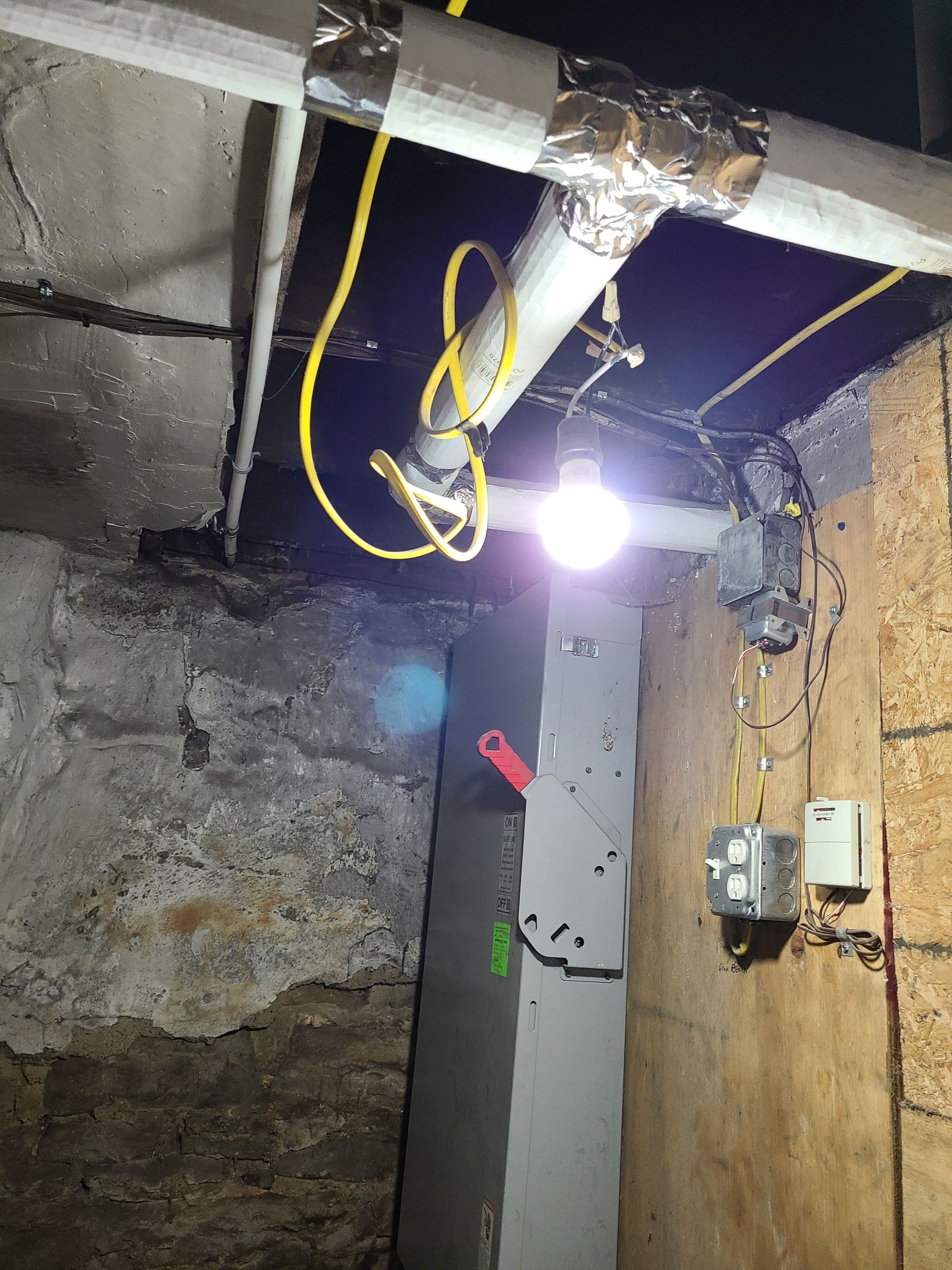 Basement interior with exposed pipes, electrical wiring, and a lightbulb.