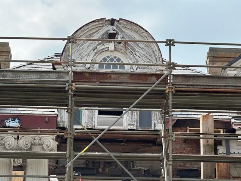 Building facade with scaffolding, undergoing renovation. White dome with peeling paint, arched window.