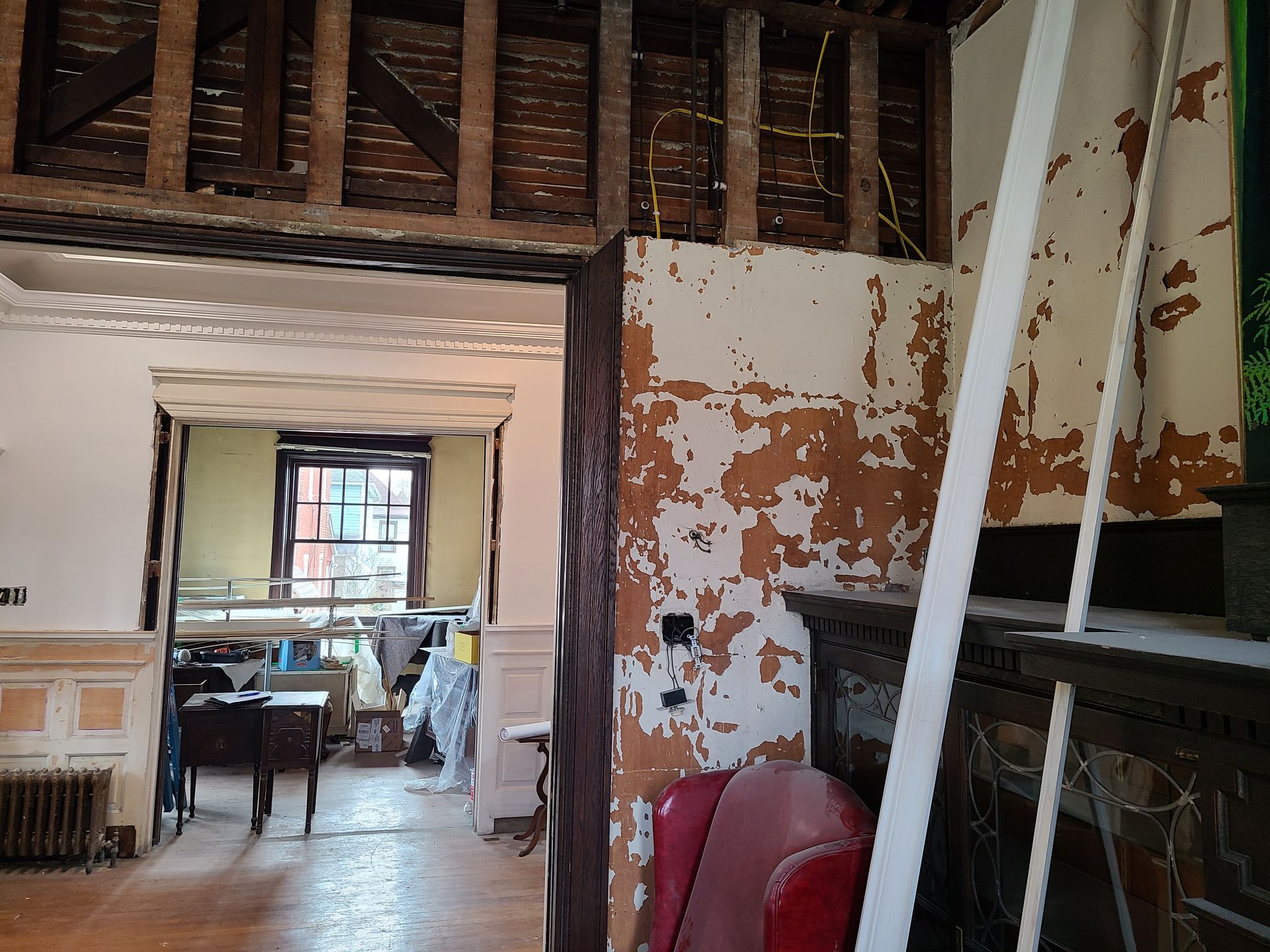 Interior renovation: exposed beams, peeling walls, doorway to a room with window.