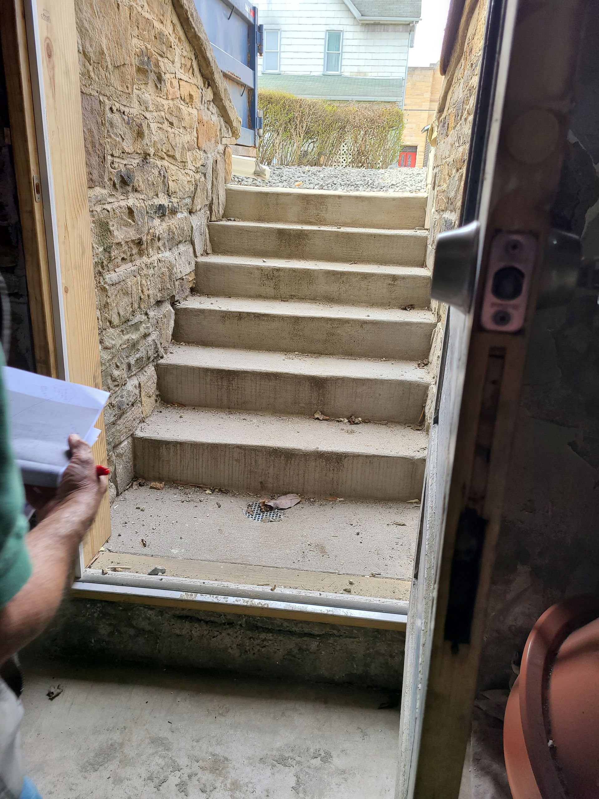 Concrete stairs leading upwards from an interior doorway. Stone walls are to the left, and a partially open door is on the right.