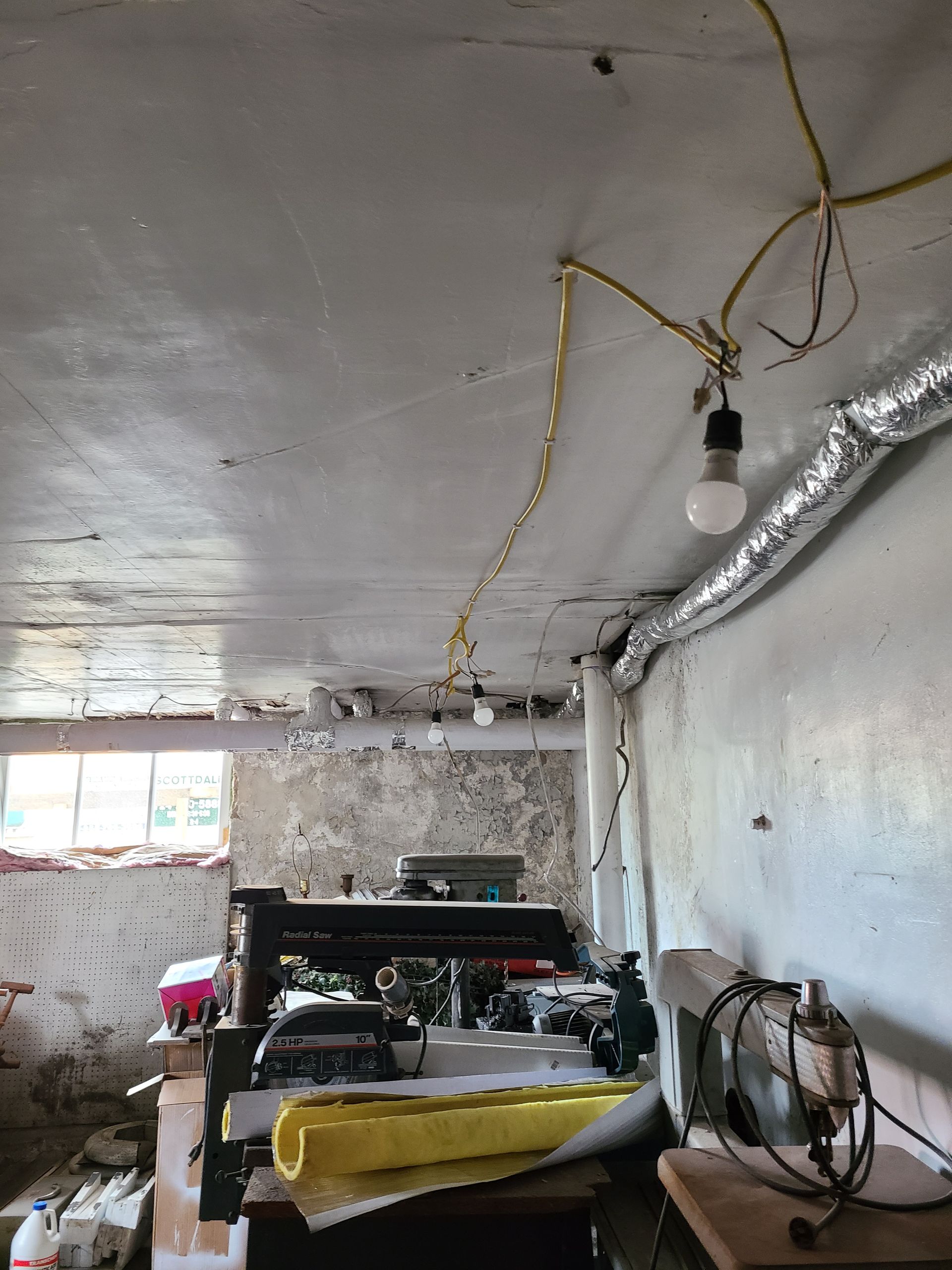 Basement with exposed wiring and a bare bulb hanging from the ceiling.