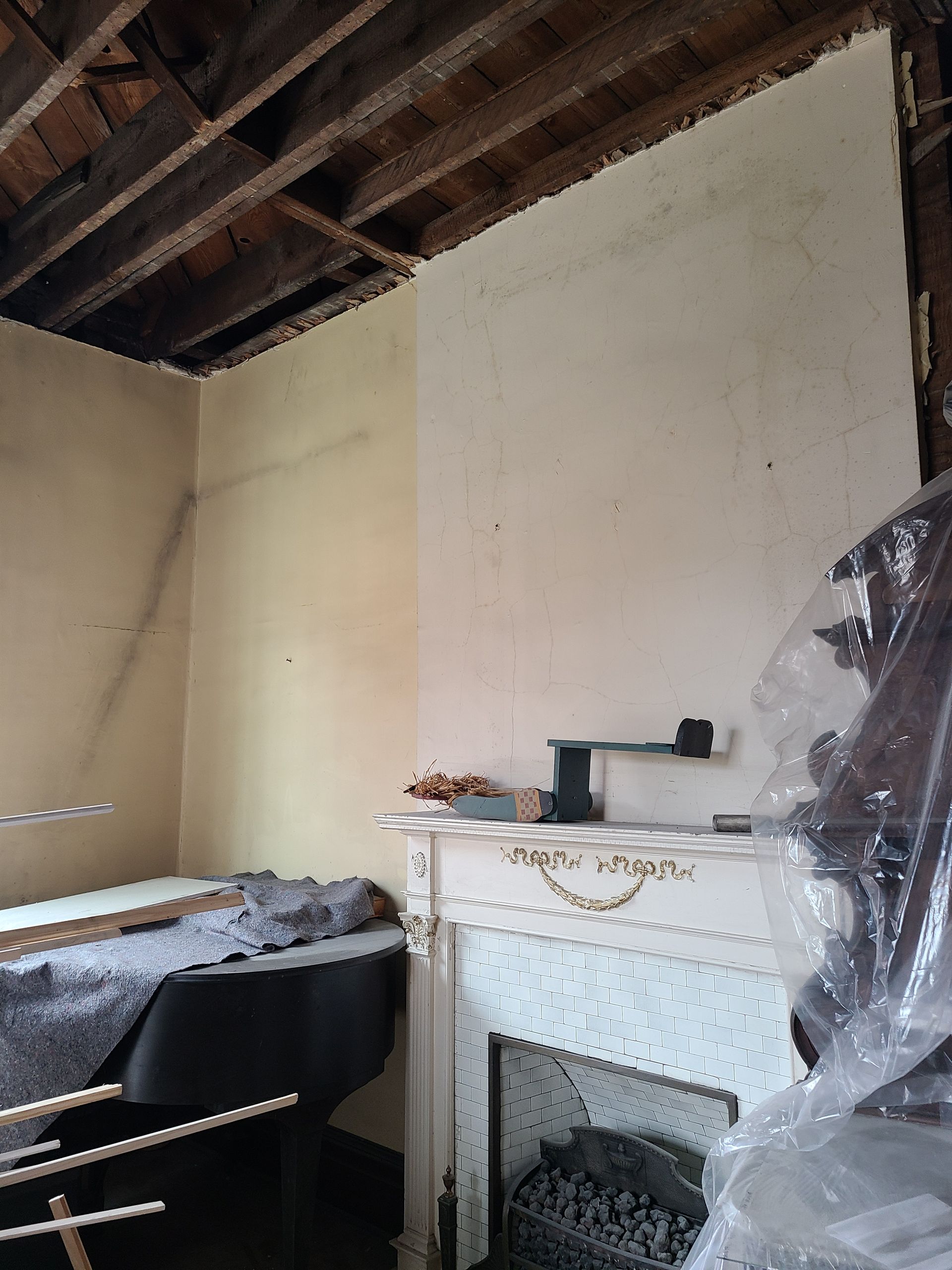 Room with a fireplace and exposed ceiling beams during renovation. Walls are painted light colors.