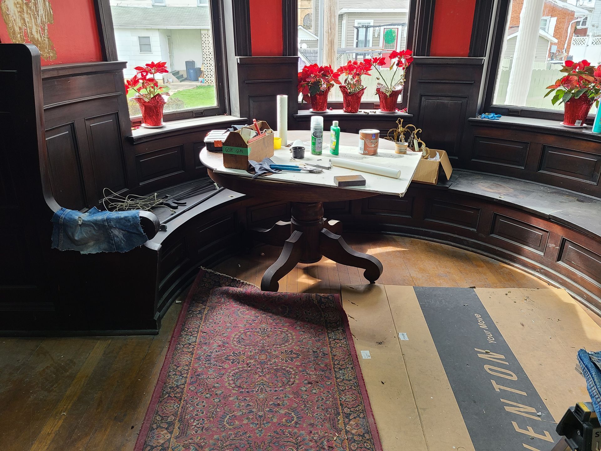 Room with curved wooden bench, round table, and windows decorated with red poinsettias.