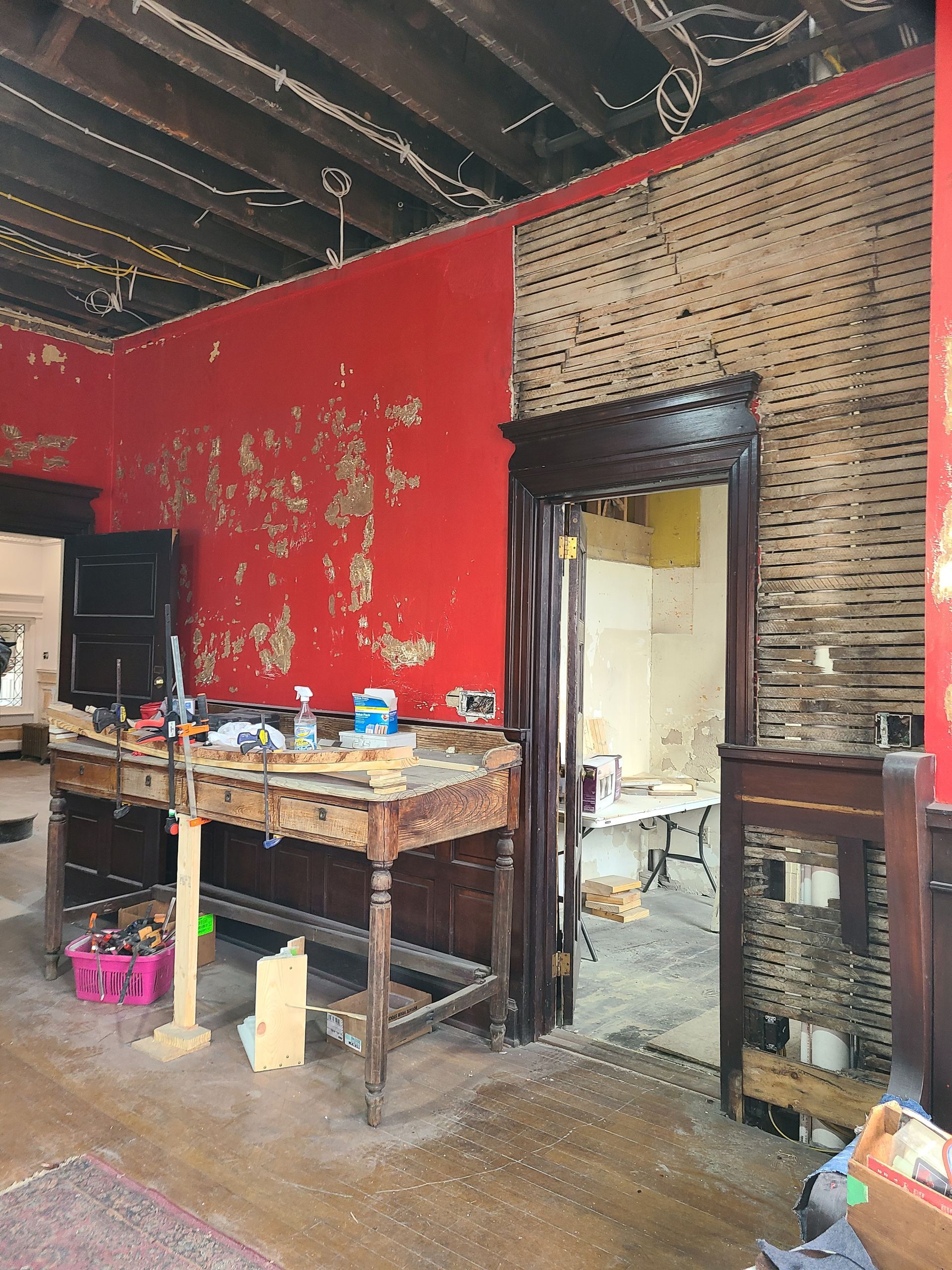 Room interior undergoing renovation with exposed framing, red walls, and a wooden work table.