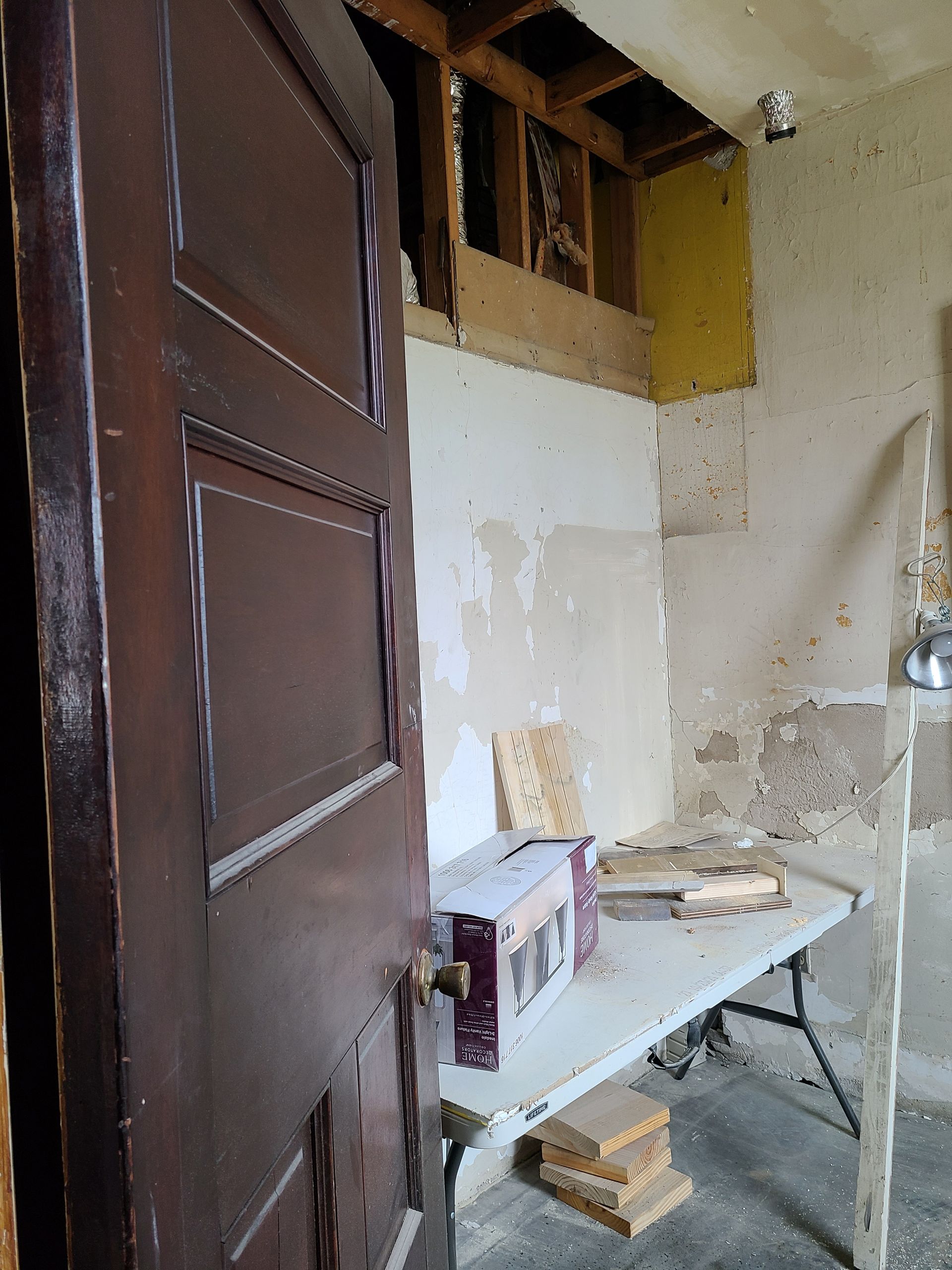 Brown door open to a room with exposed wall and ceiling, a table, and debris.