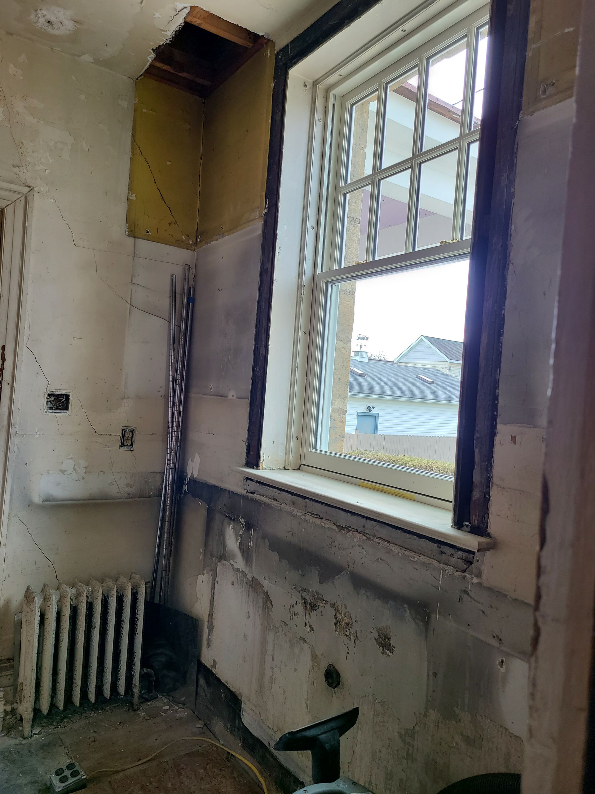 Interior view of a room under renovation, with a window, radiator, and exposed wall materials.