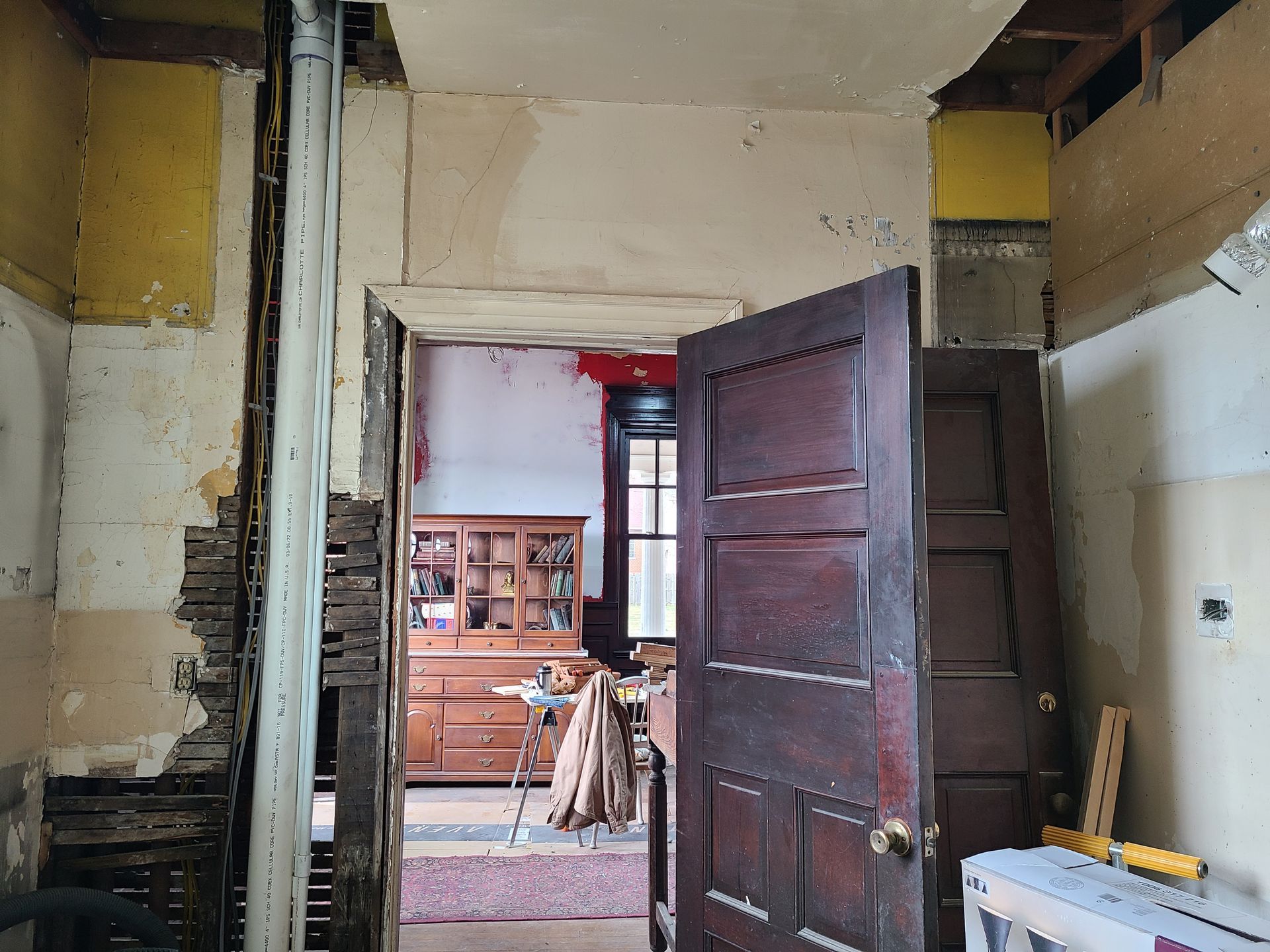 Interior doorway with exposed wall studs, leading to a room with furniture.