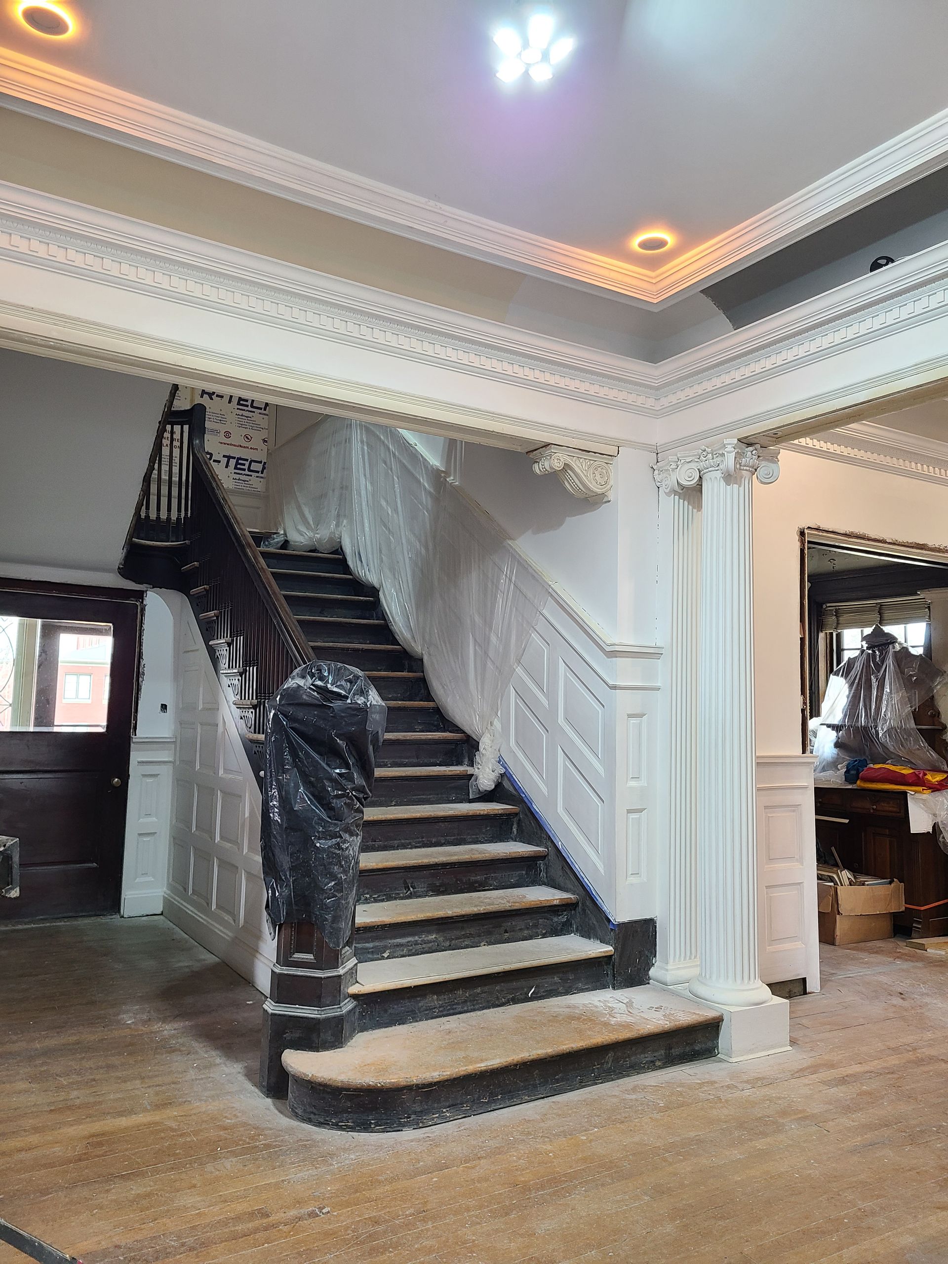 Staircase with ornate white molding and dark wooden banister. Entryway with wood floors, light fixtures.