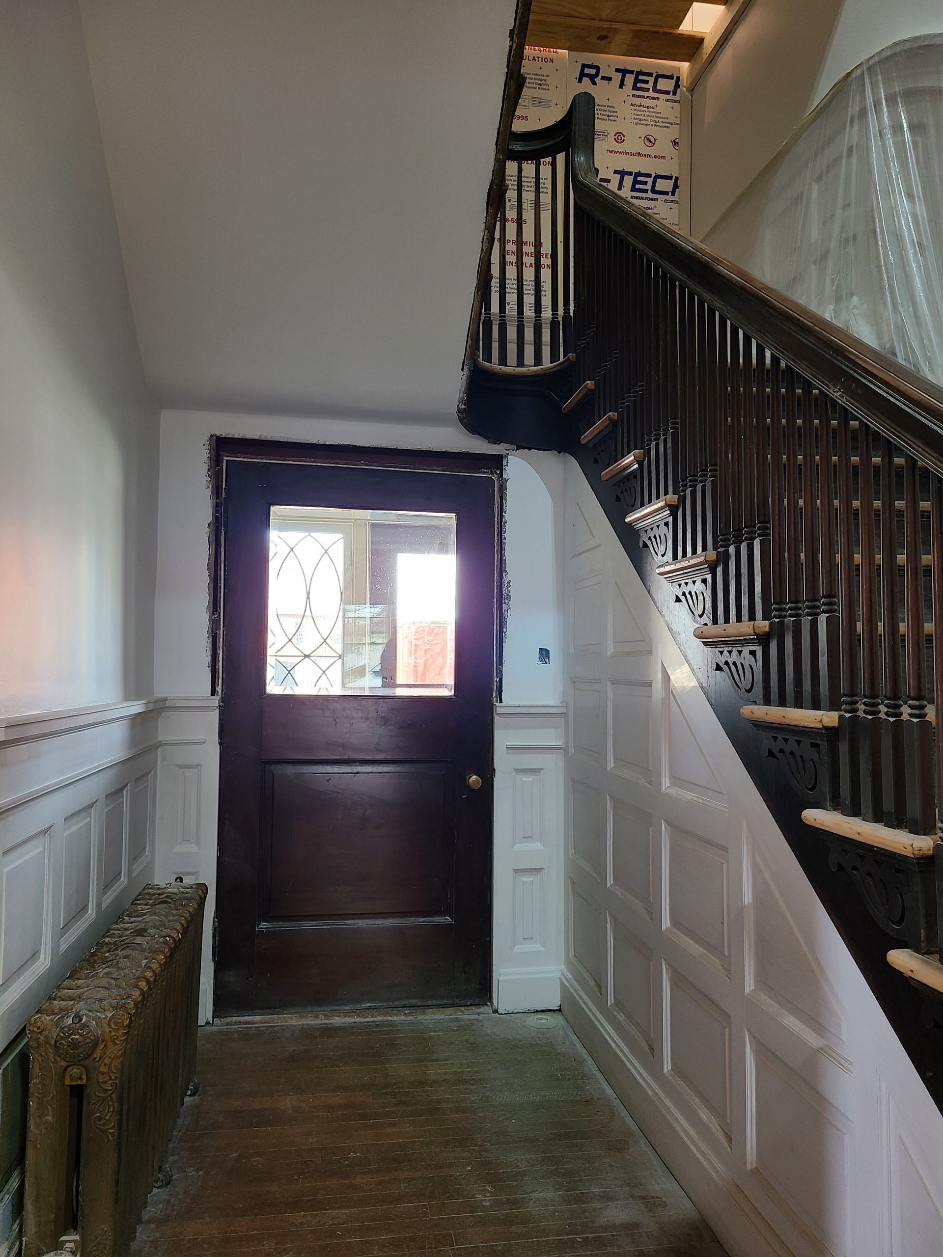 Entryway with wooden door, staircase, wainscoting, and radiator.