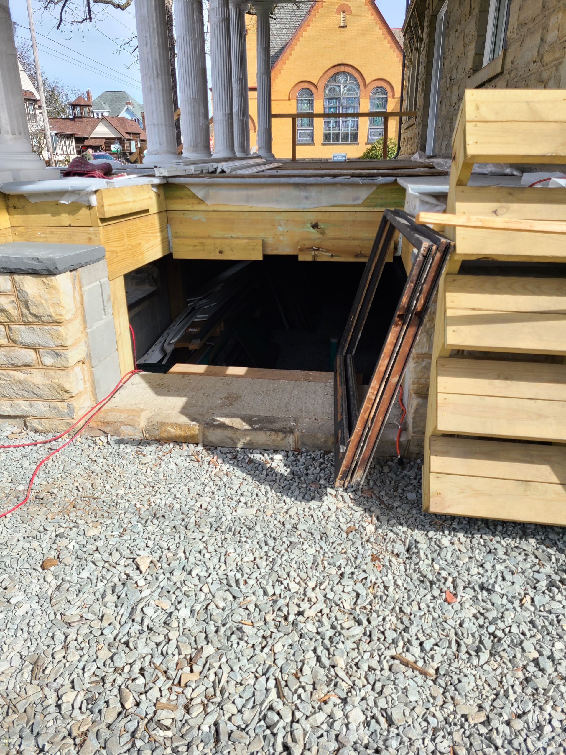 Construction site. Wooden porch with exposed under-structure and access point. Gravel ground.
