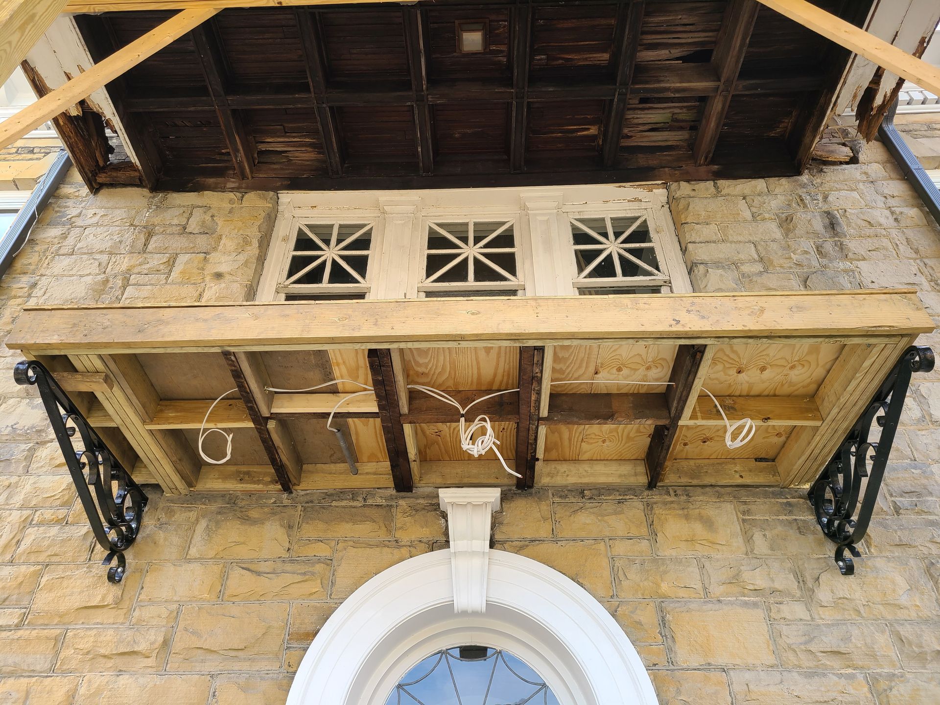 Stone building facade with a small wooden balcony and three arched windows.