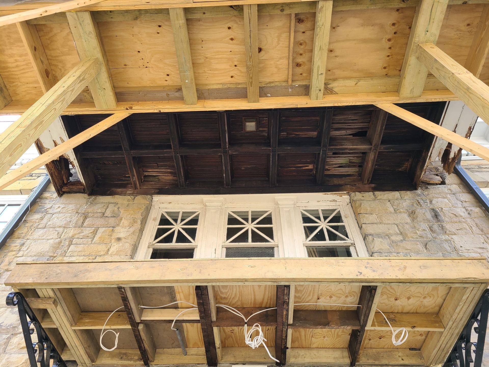Exterior view of a building with a porch. The porch roof is under repair. A row of windows is below the porch.