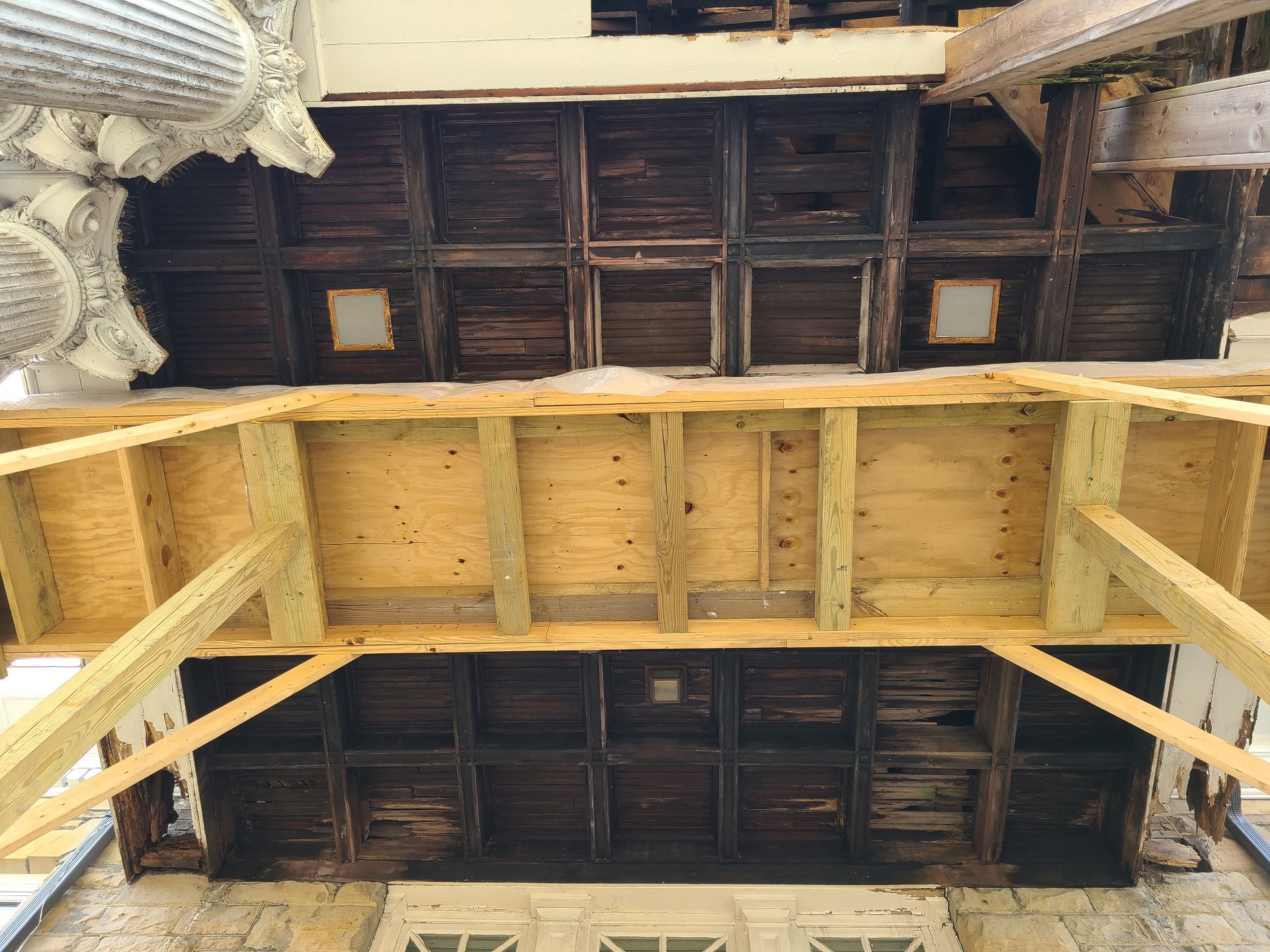 Wooden ceiling with damage, under construction with scaffolding. New wood supports old structure.