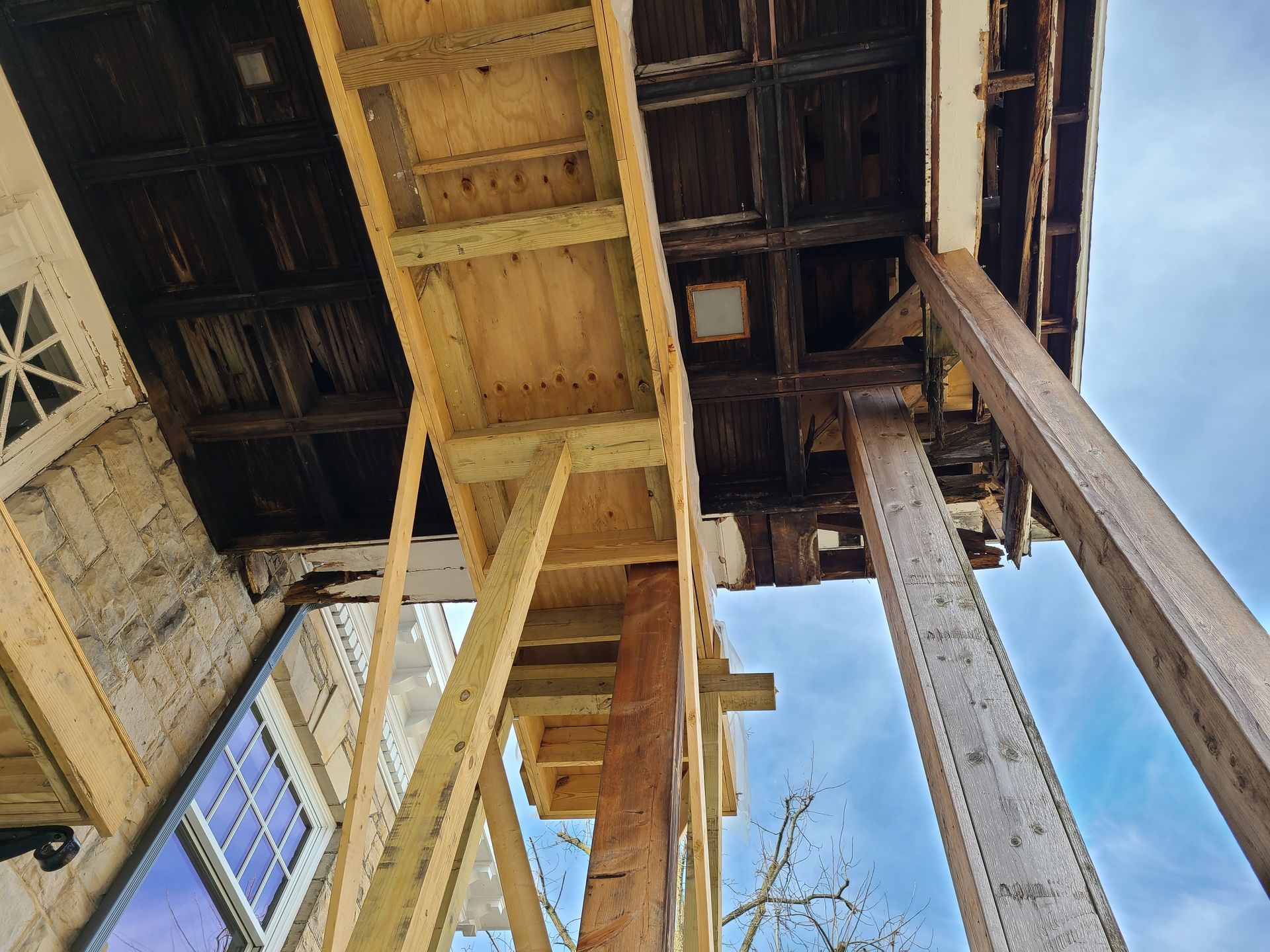 Wooden supports hold up a decaying building's overhang. Visible is the underside of the roof and a window.