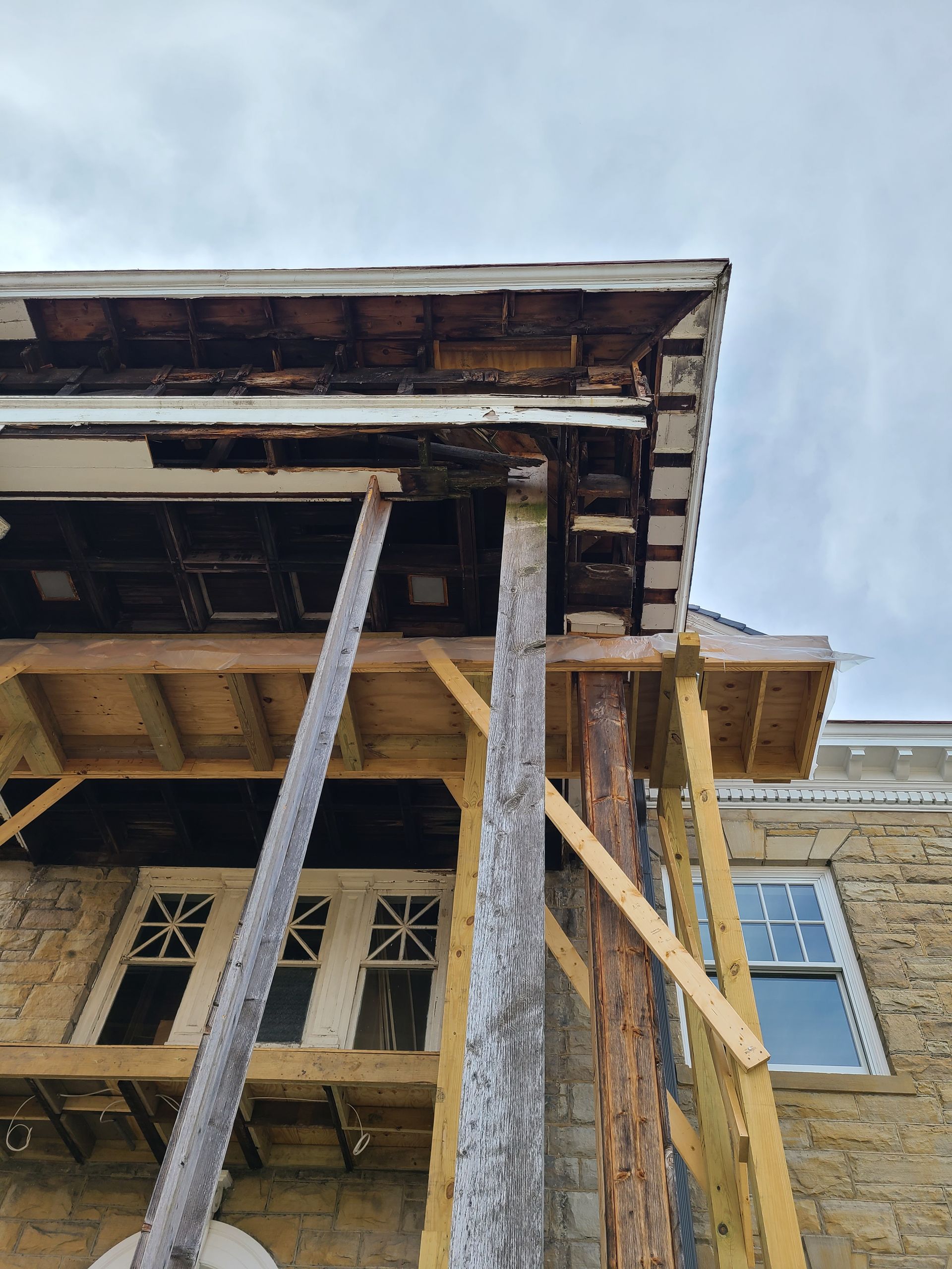 Building facade under construction, wood supports holding up roof, cloudy sky.