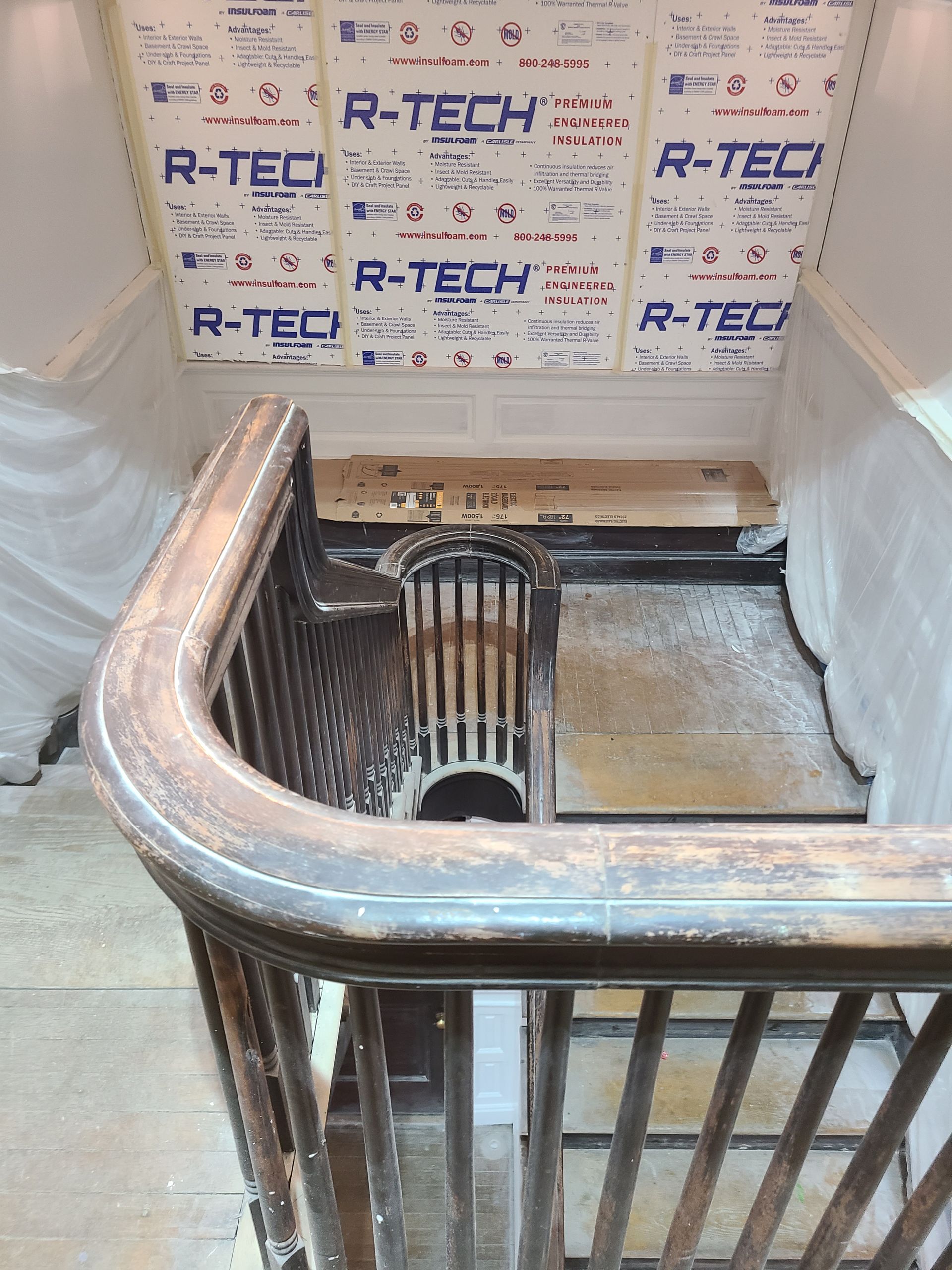 Staircase with wooden railing and insulation on the ceiling; construction in progress.