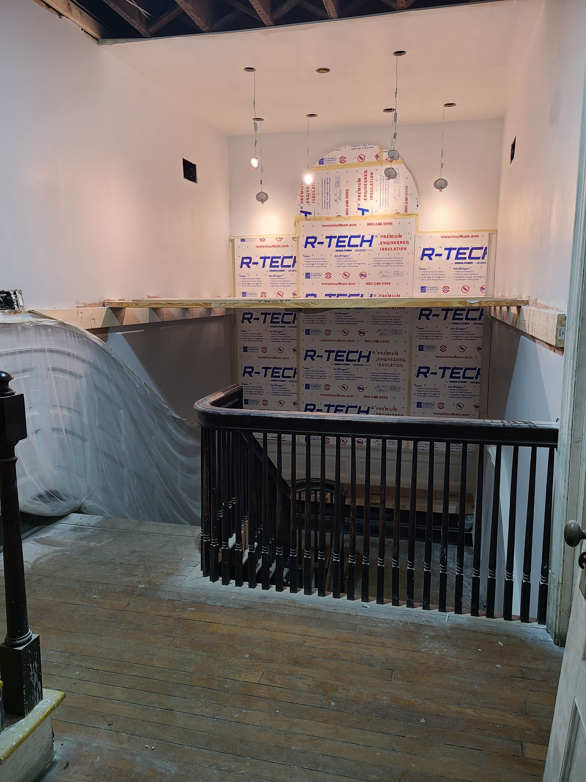 Interior construction site with stairs, a railing, and insulation on the walls.