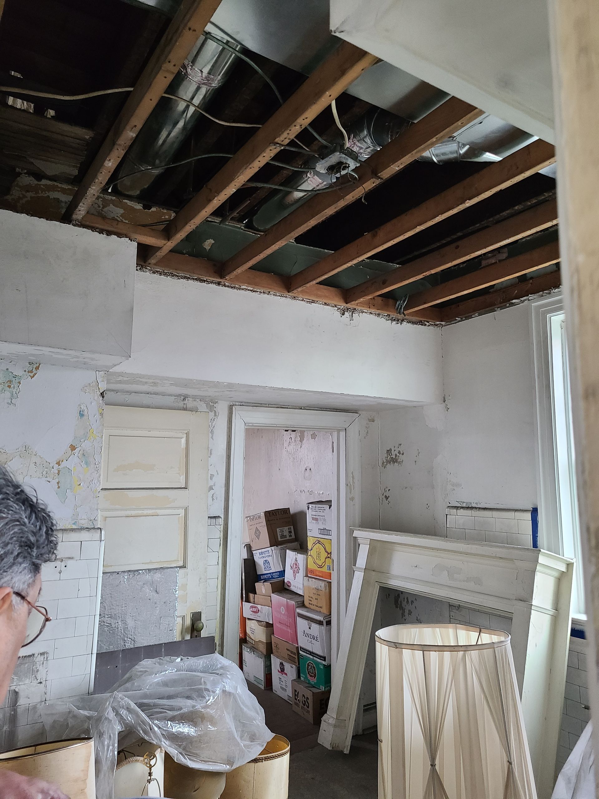 Room under renovation: exposed ceiling beams, doorway, fireplace, and lamp.