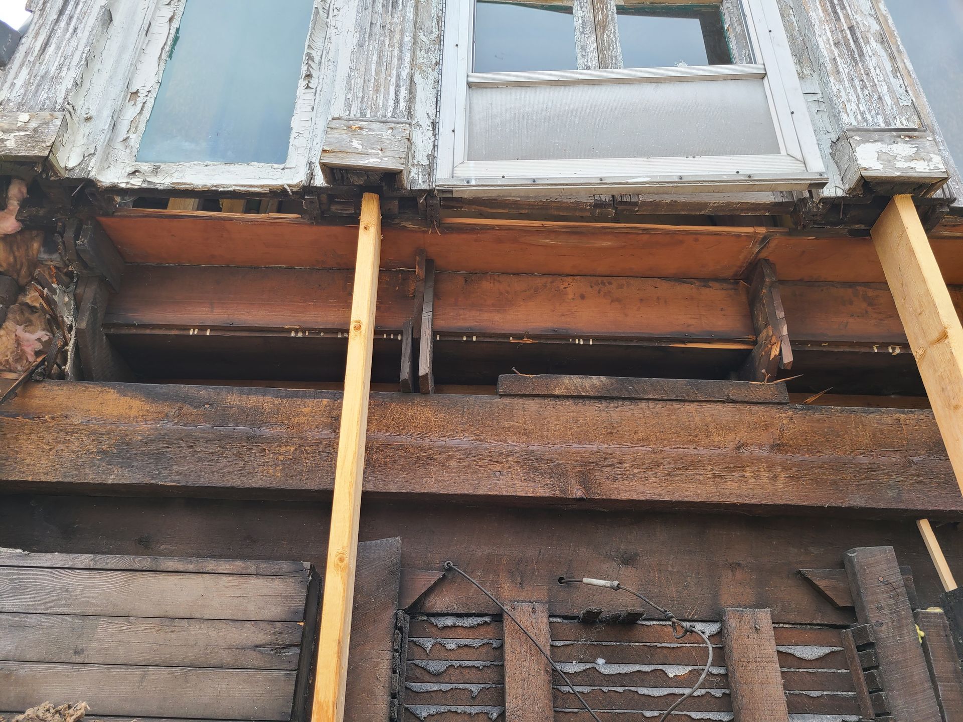 Exterior of a building under renovation, showing exposed beams, weathered wood, and supporting wooden posts.
