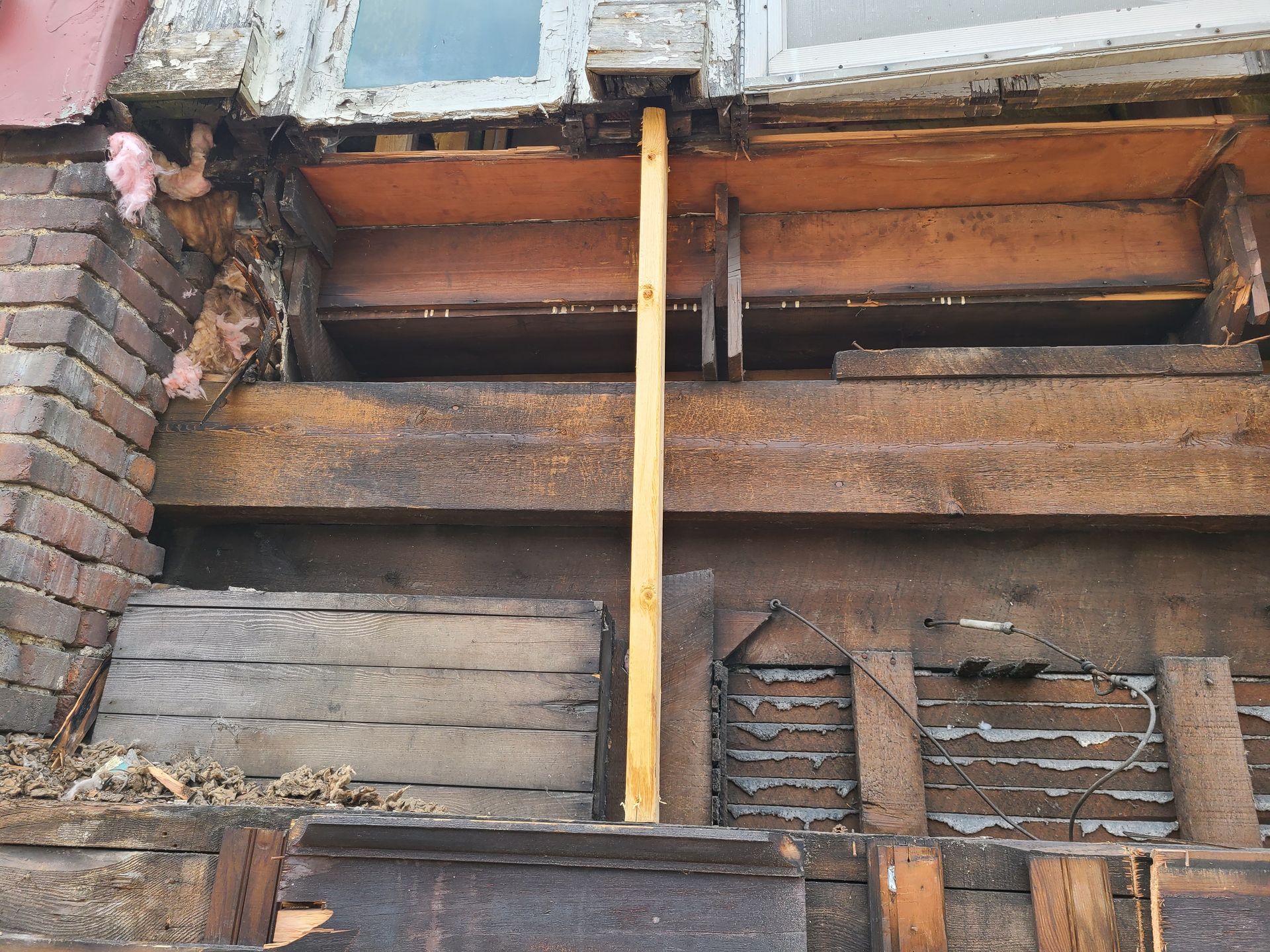 Exposed window frame with brick, wood, and a supporting post, showing structural damage.
