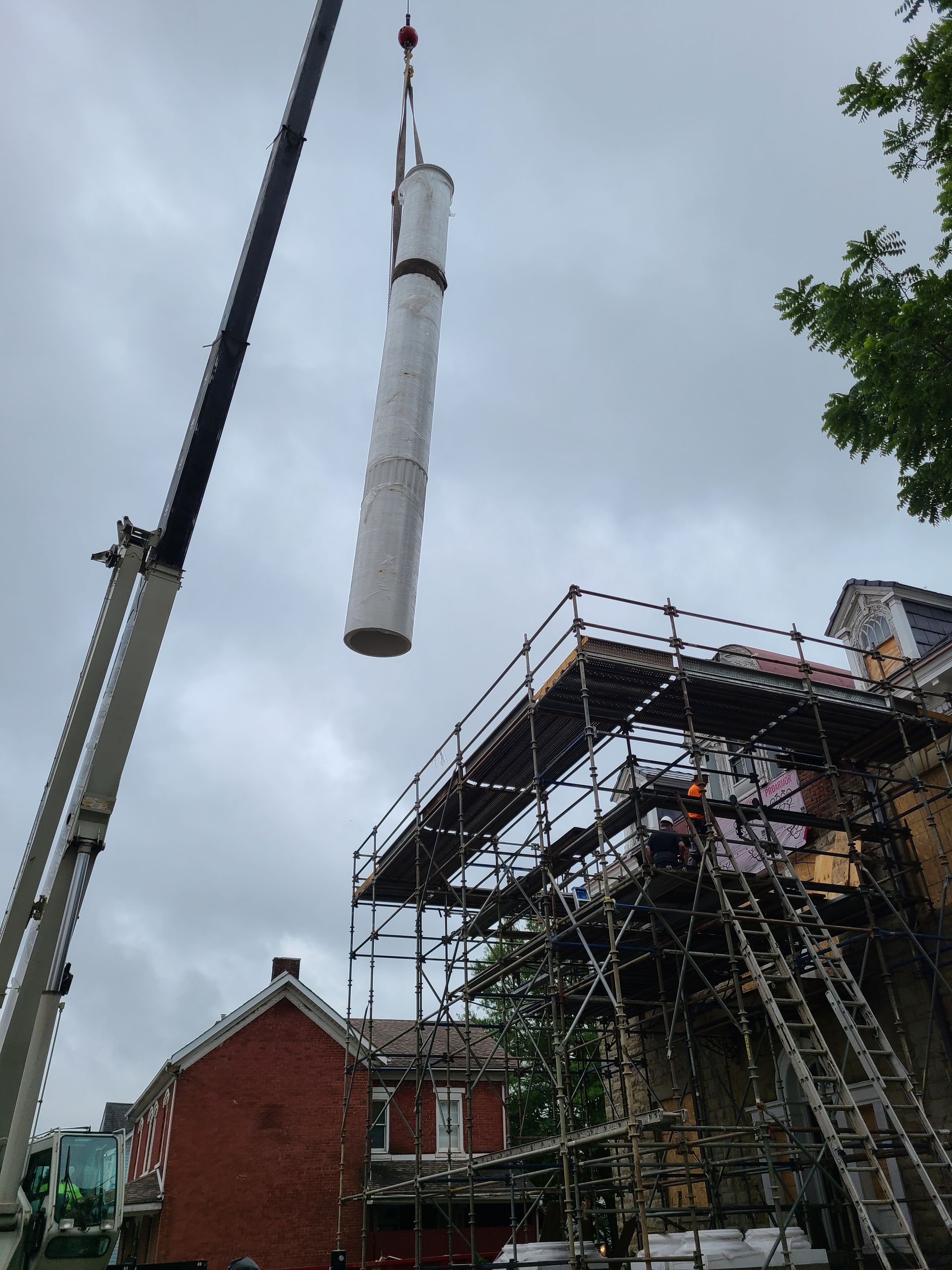 A crane lifting a long cylindrical object over a building with scaffolding. Cloudy sky.
