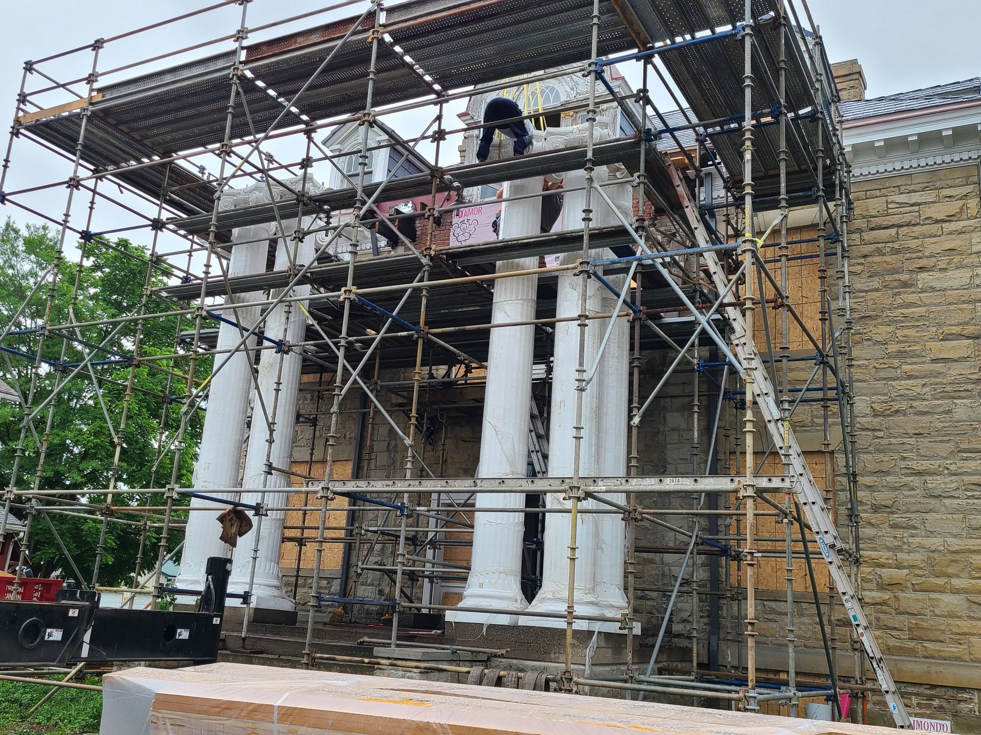 Facade with white columns, under scaffolding, during restoration work. A person is visible on top.