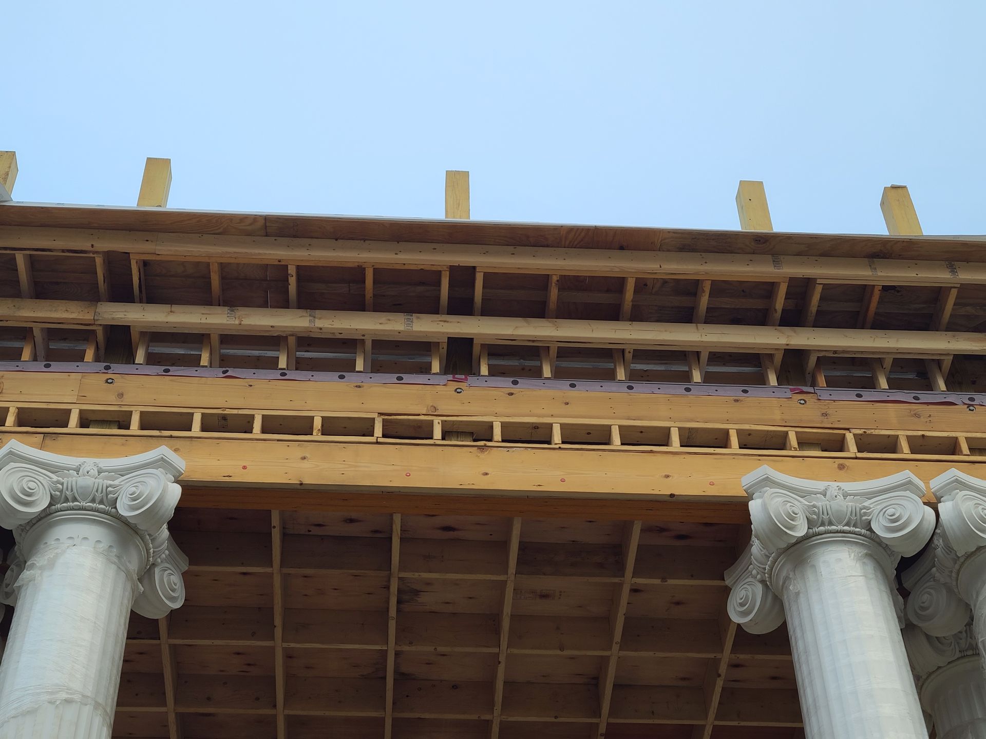 Columns supporting a wooden structure with a grid ceiling, topped by a light blue sky.