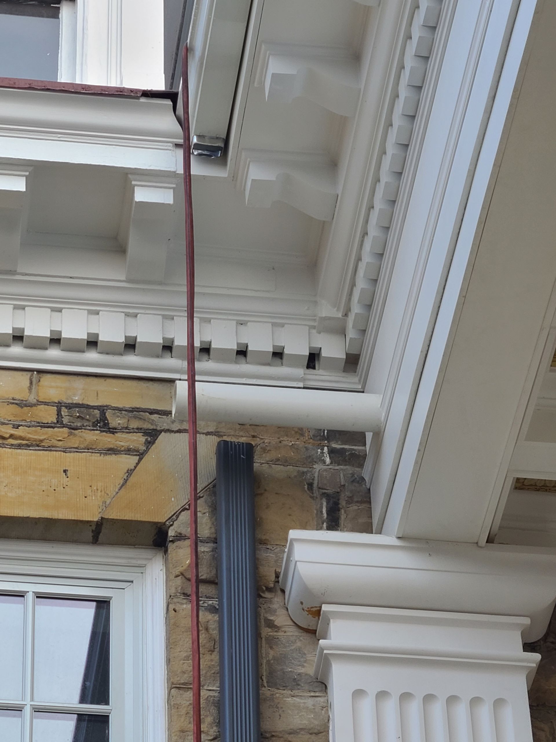 Close-up of a building's white decorative trim and gutter system, next to a brick wall.