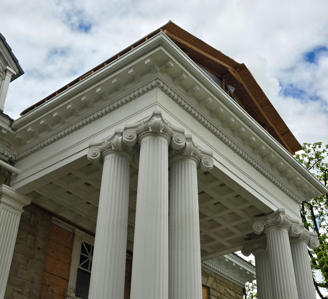 White columns supporting an ornate roof on a stone building, under a cloudy sky.
