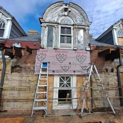 Facade of a building under renovation with scaffolding and ladders. Pinkish insulation is visible.