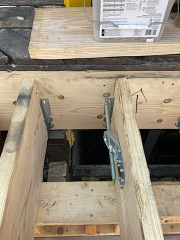 Wooden deck frame with metal brackets, tools, and a dark space beneath.